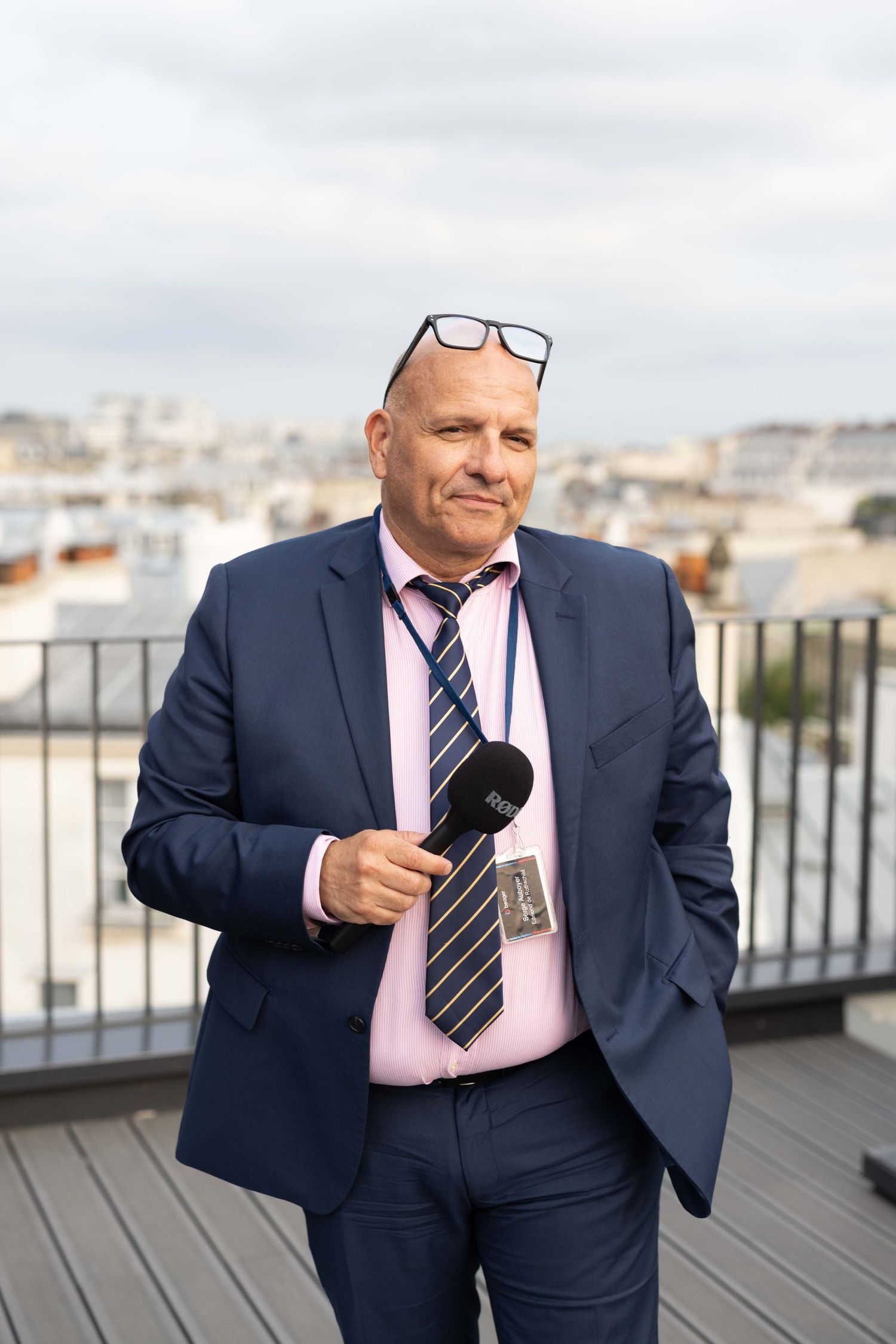 Professional in navy suit holding microphone during rooftop interview.