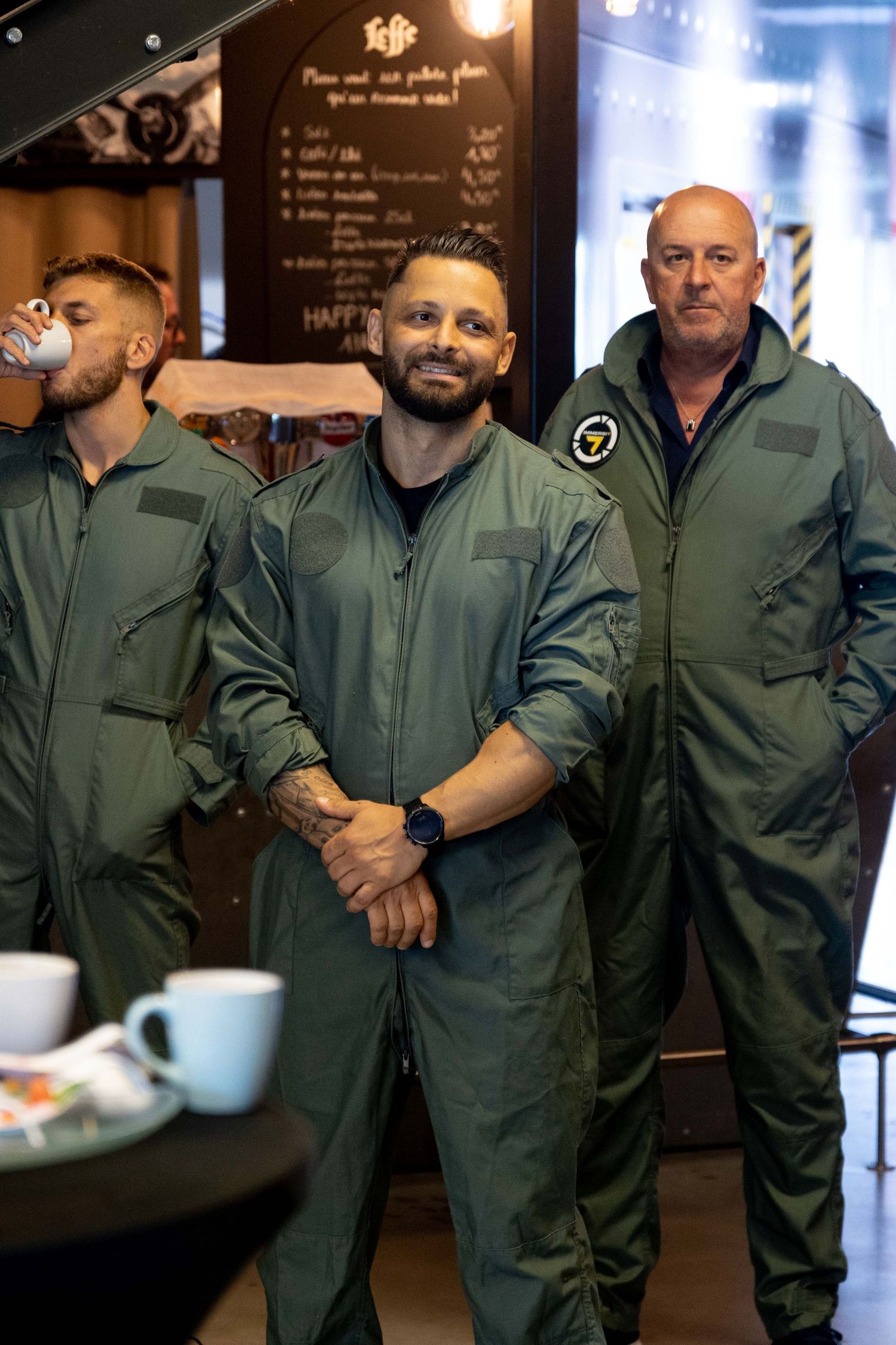 Military personnel wearing olive green flight suits gather in a casual setting.