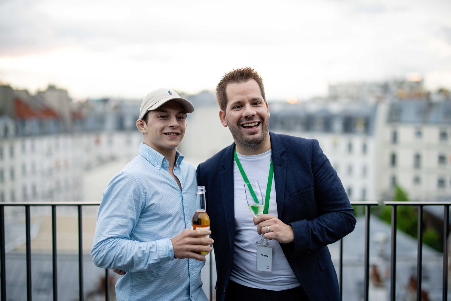 Two colleagues enjoying drinks on a rooftop terrace with Parisian buildings in background.