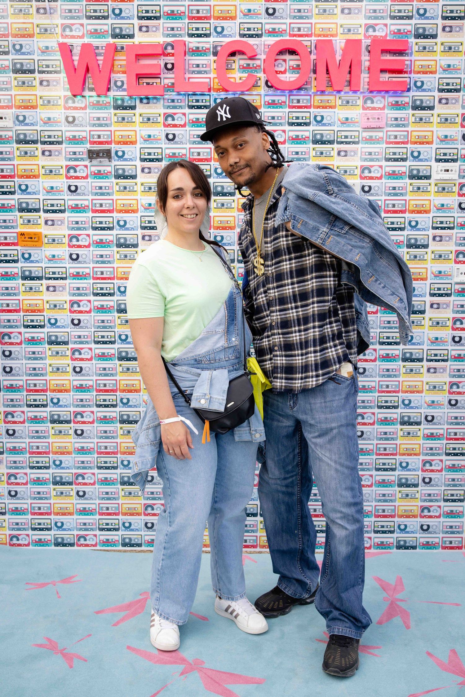 Group in casual 90s style clothing poses against wall featuring colorful cassette tape artwork.