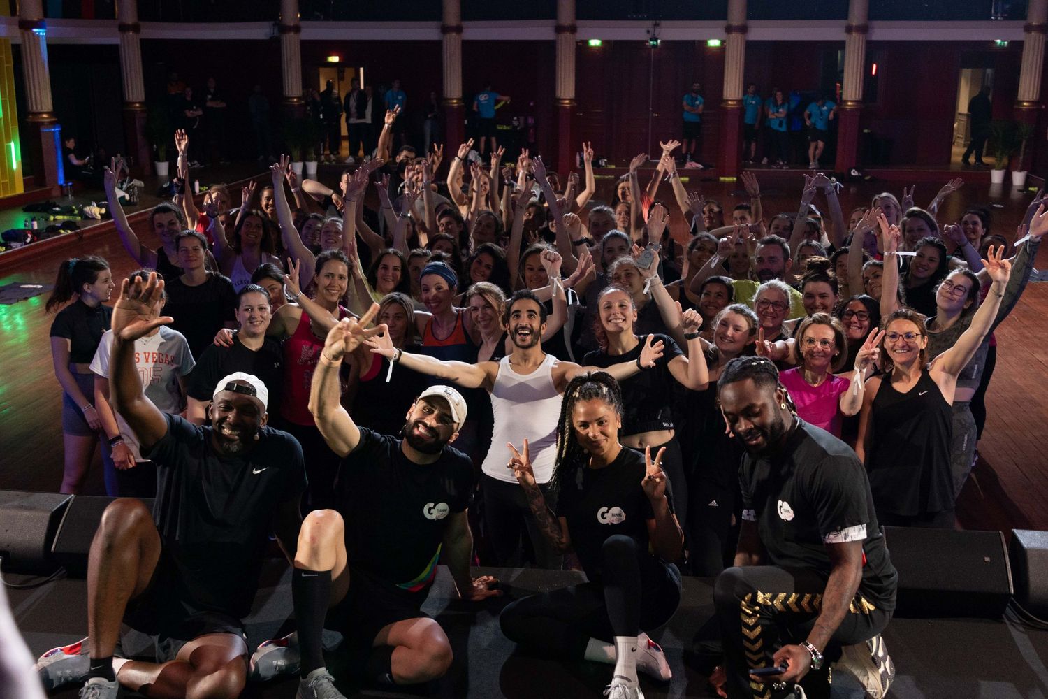 Enthusiastic crowd with raised arms at a high-energy fitness event with dramatic lighting.