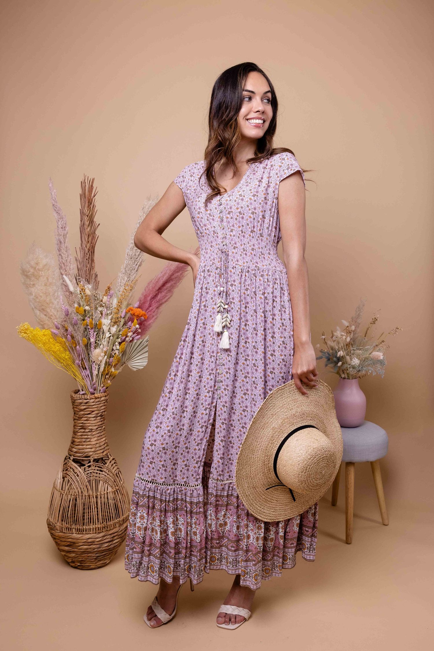 Une femme en robe fleurie lavande pose avec un chapeau de paille et des compositions de fleurs séchées.