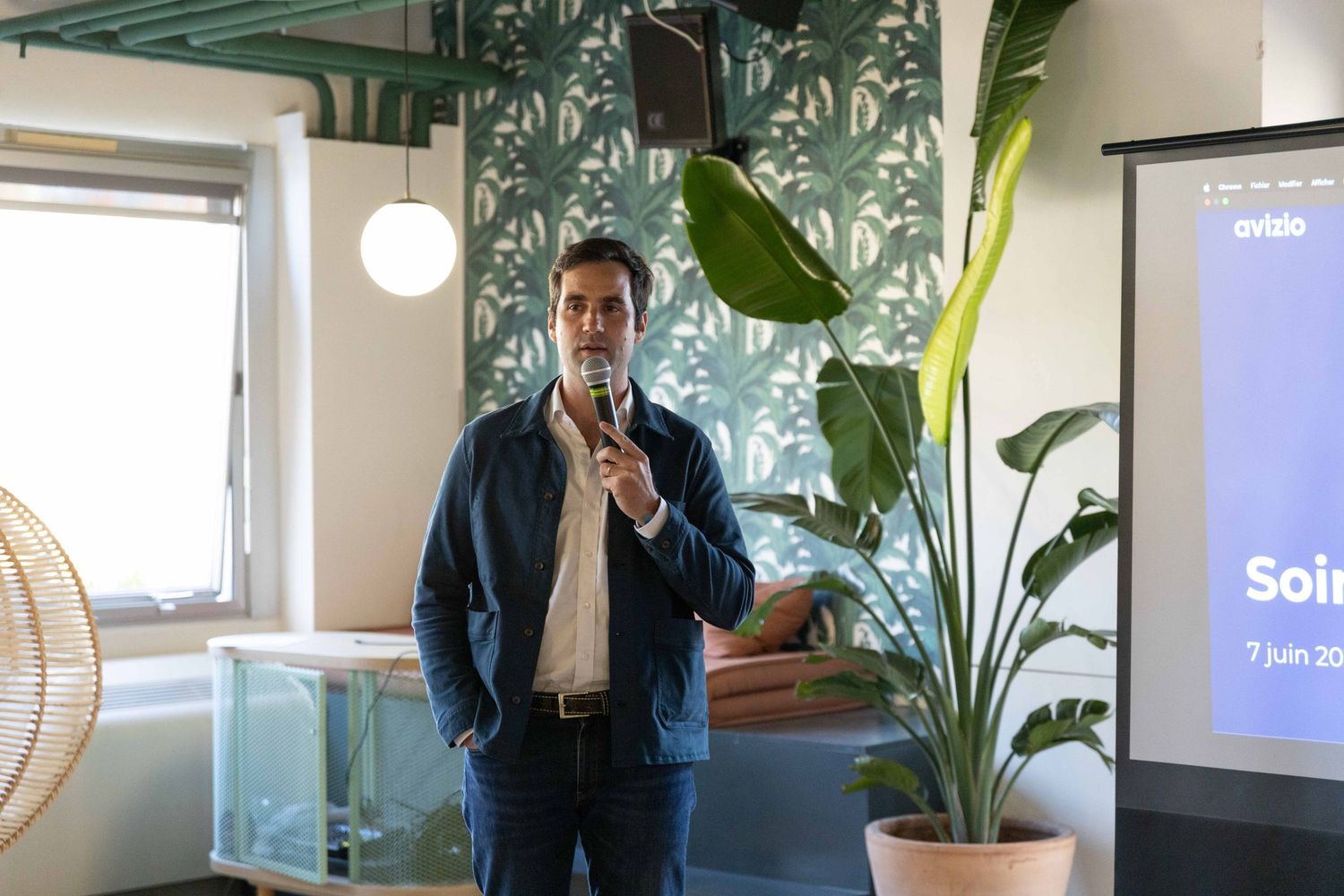 Modern office space with tropical plants and presentation screen visible in background.