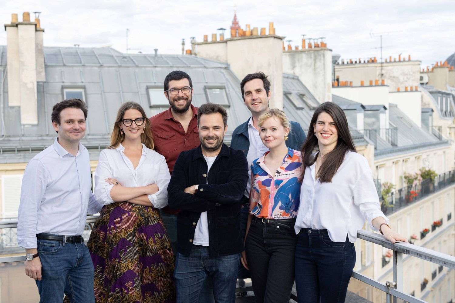 Group of people posing together on rooftop with Parisian skyline in background.