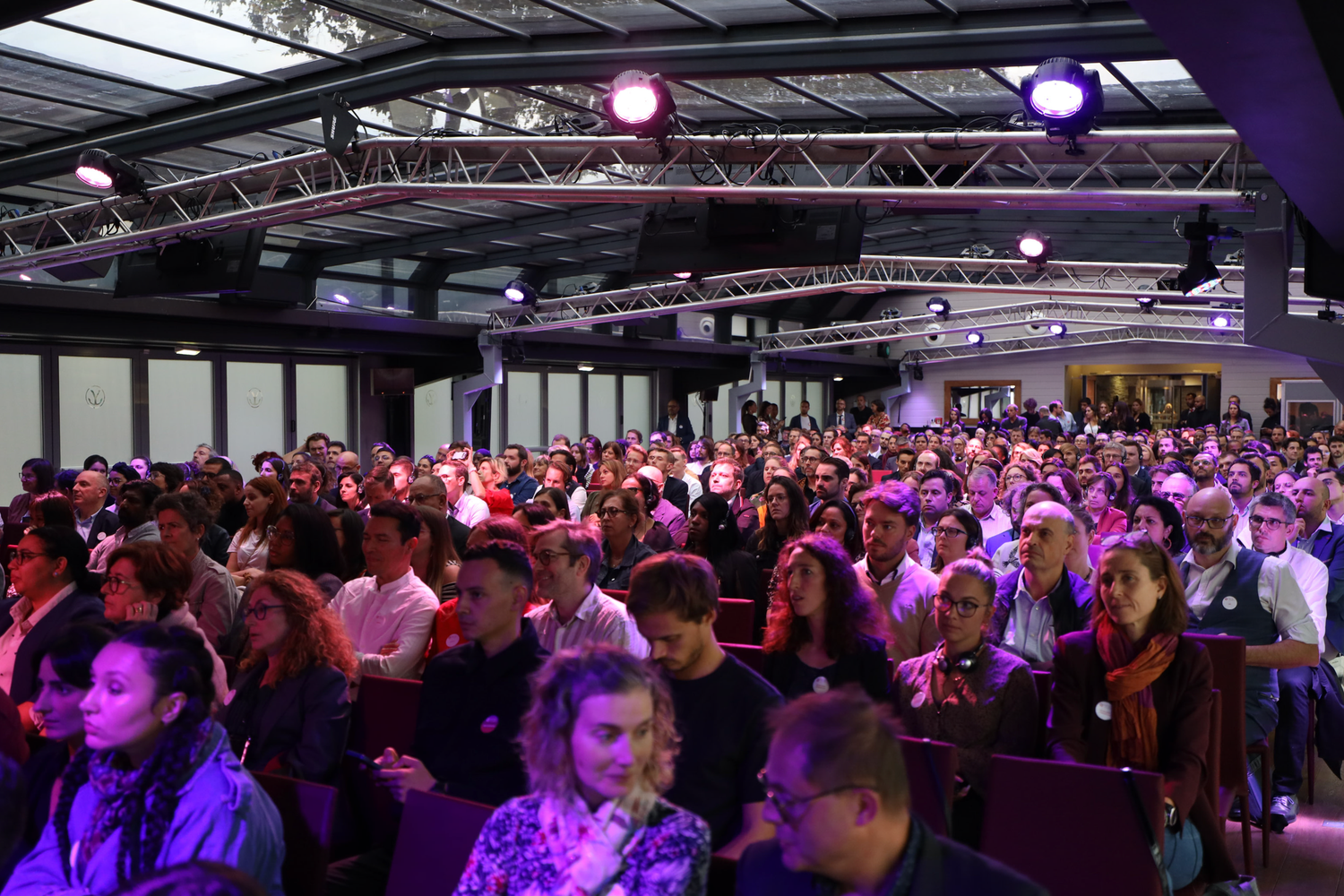 Crowded conference hall filled with attendees under purple ambient lighting.
