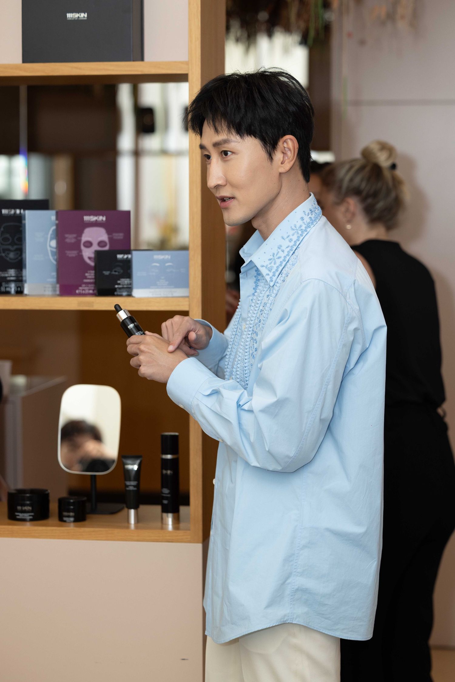 Person in light blue shirt examining products on wooden shelving unit.