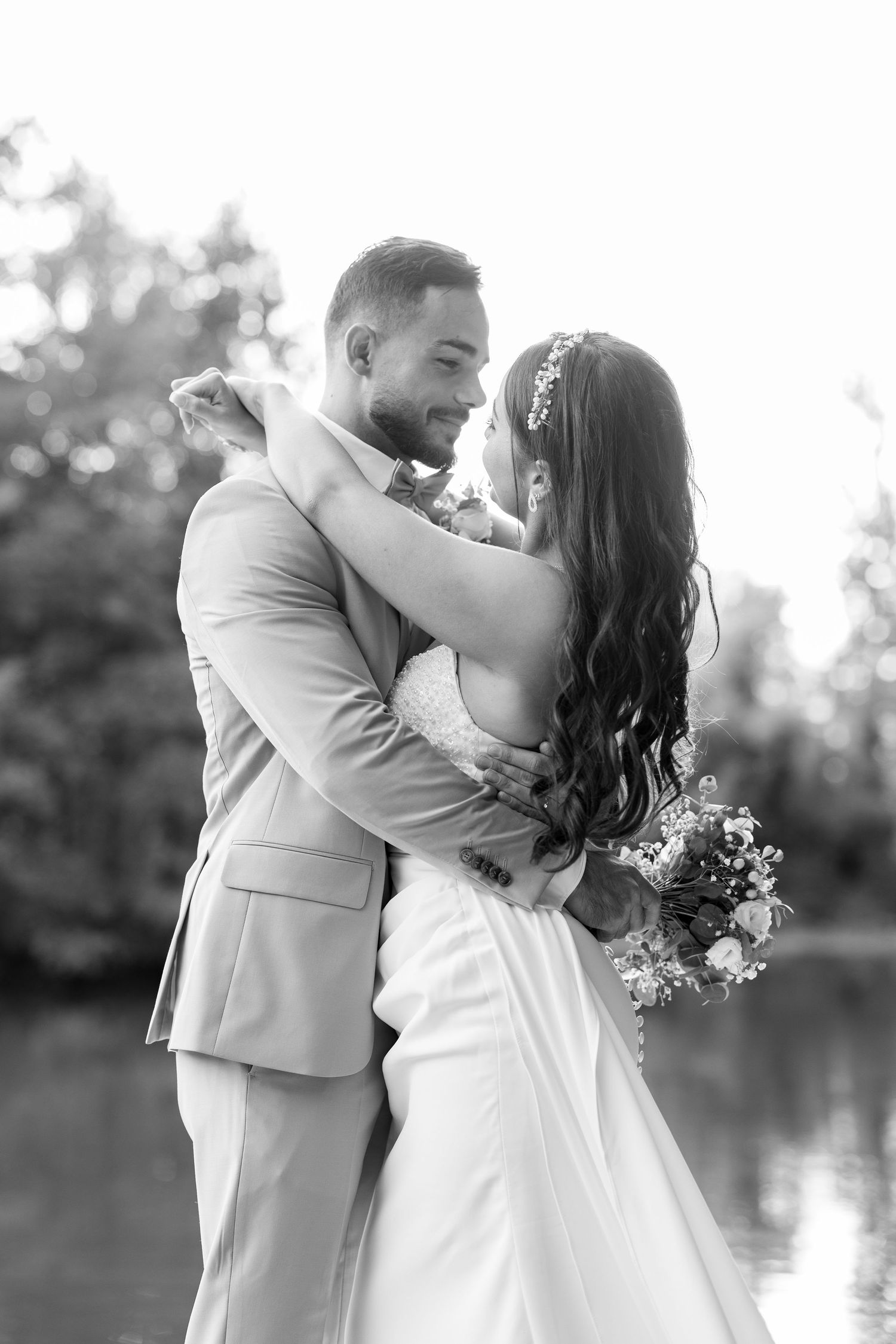 A romantic black and white wedding photo series shows a couple sharing intimate kisses by a lakeside.