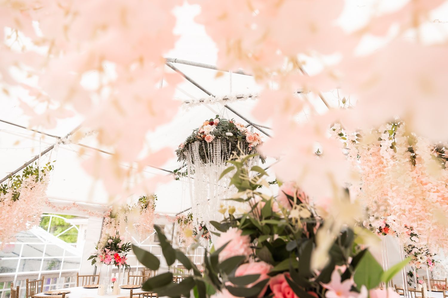 Dreamy view of wedding tent ceiling with hanging decorations and soft pink lighting.