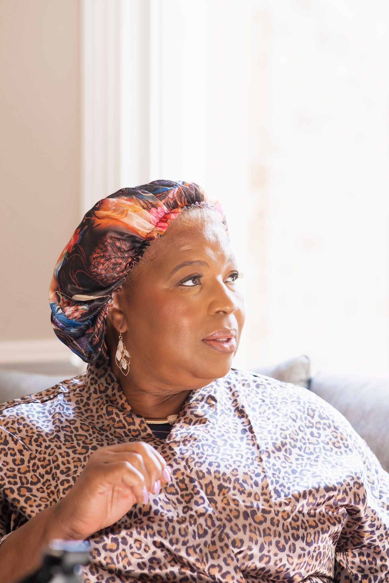 Woman wearing colorful headwrap and leopard print blouse gazing to the side in soft natural light.
