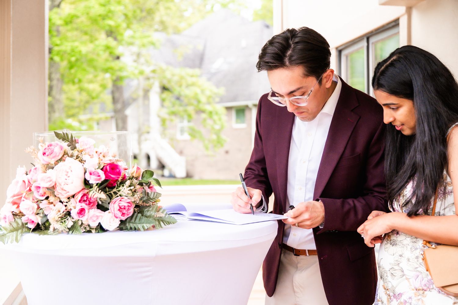 Wedding couple signing documents at an elegant table with pink floral arrangements.