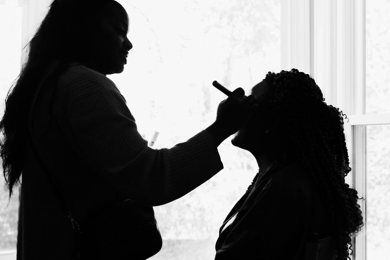 Silhouette of stylist working on client's hair near window.