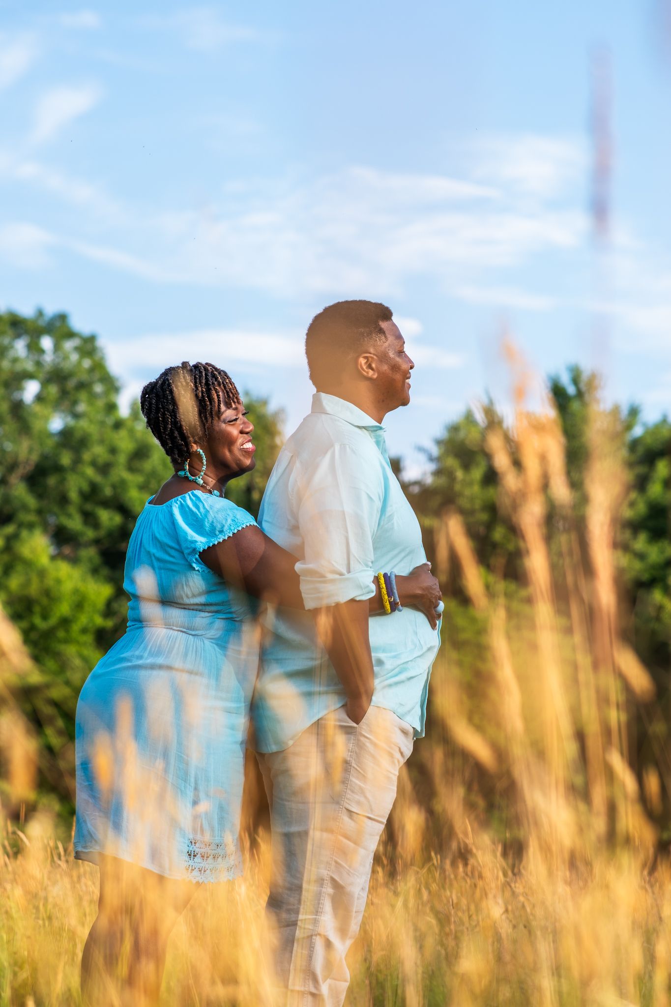 Couple standing back to back in a golden field during sunset.