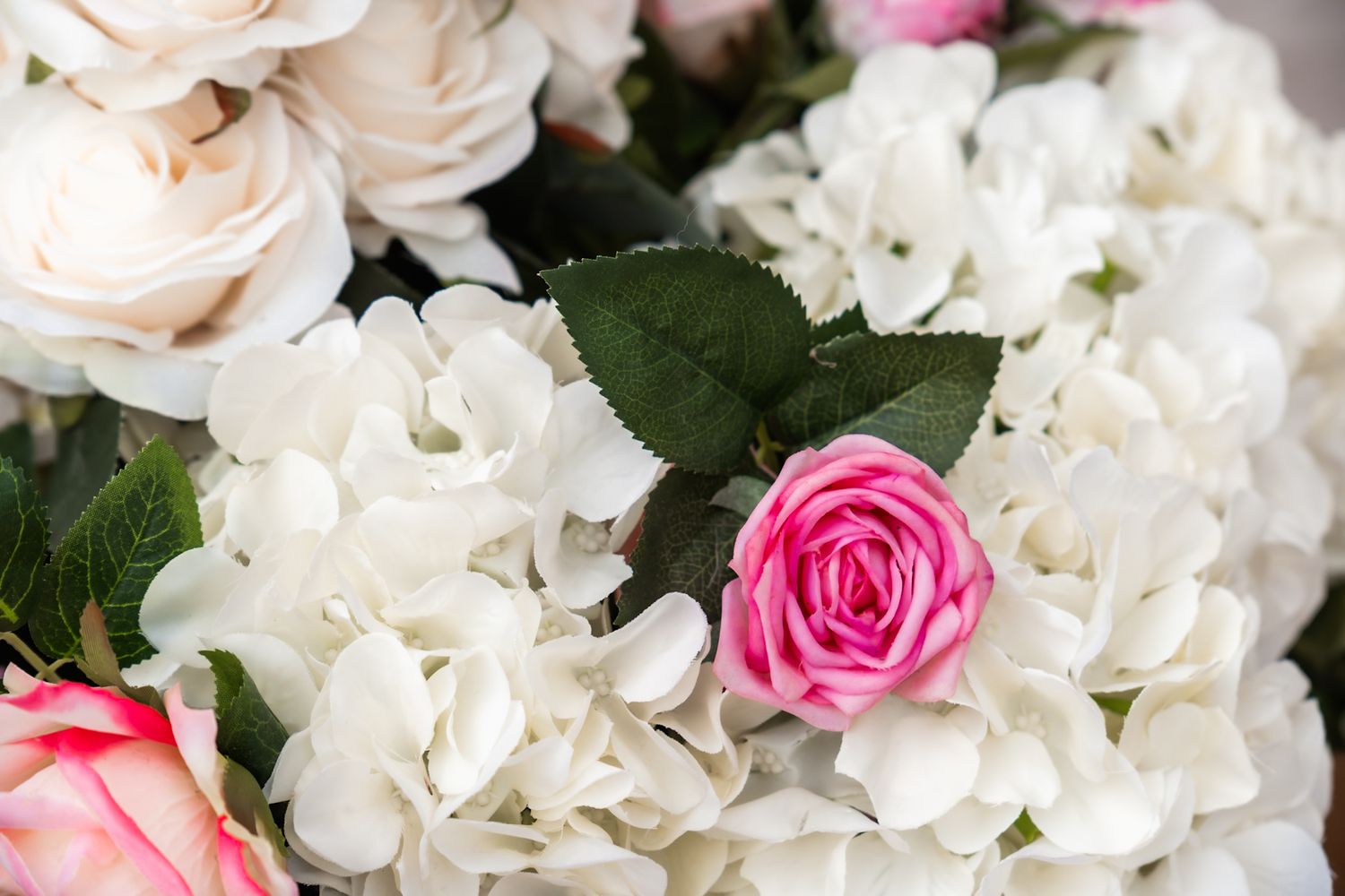 Close-up of white hydrangeas and pink roses in elegant wedding floral arrangement.
