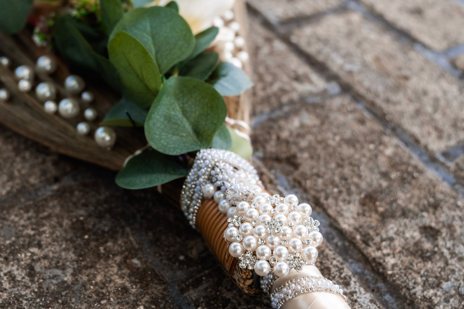 Wedding bouquet wrap decorated with pearls and rhinestones against a stone surface.