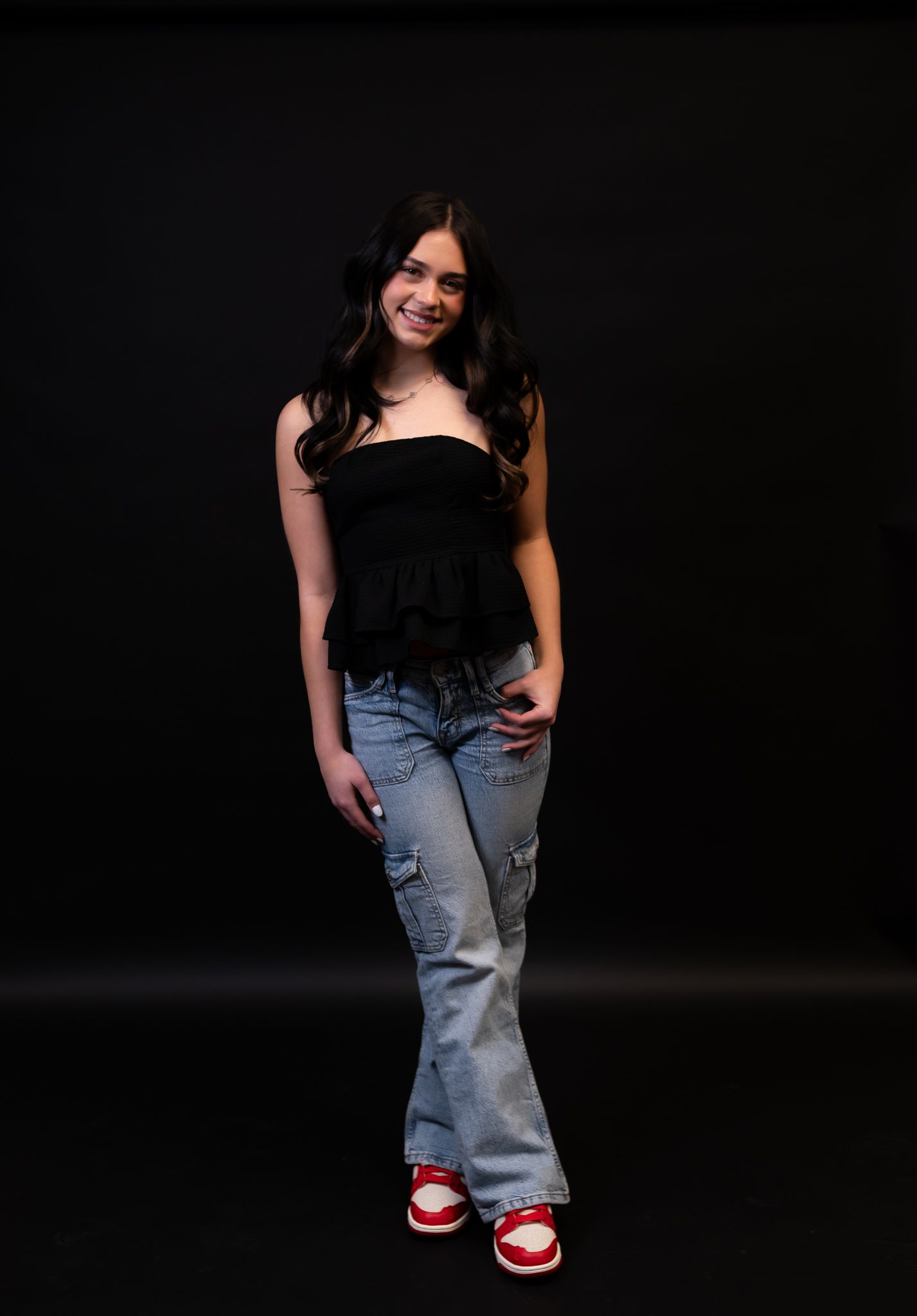 Casual portrait in black top and distressed jeans against dark background.