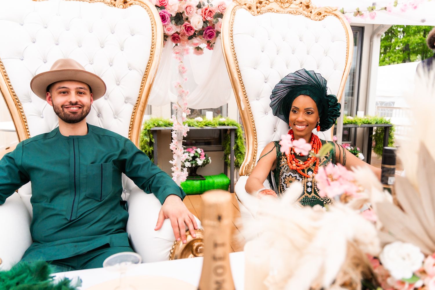 A couple sits on ornate chairs at their wedding reception.