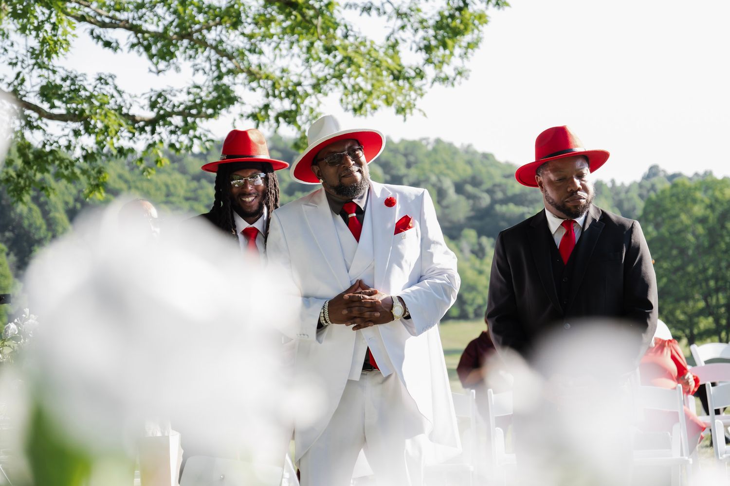 Groomsmen in white and red suits standing together during an outdoor ceremony.