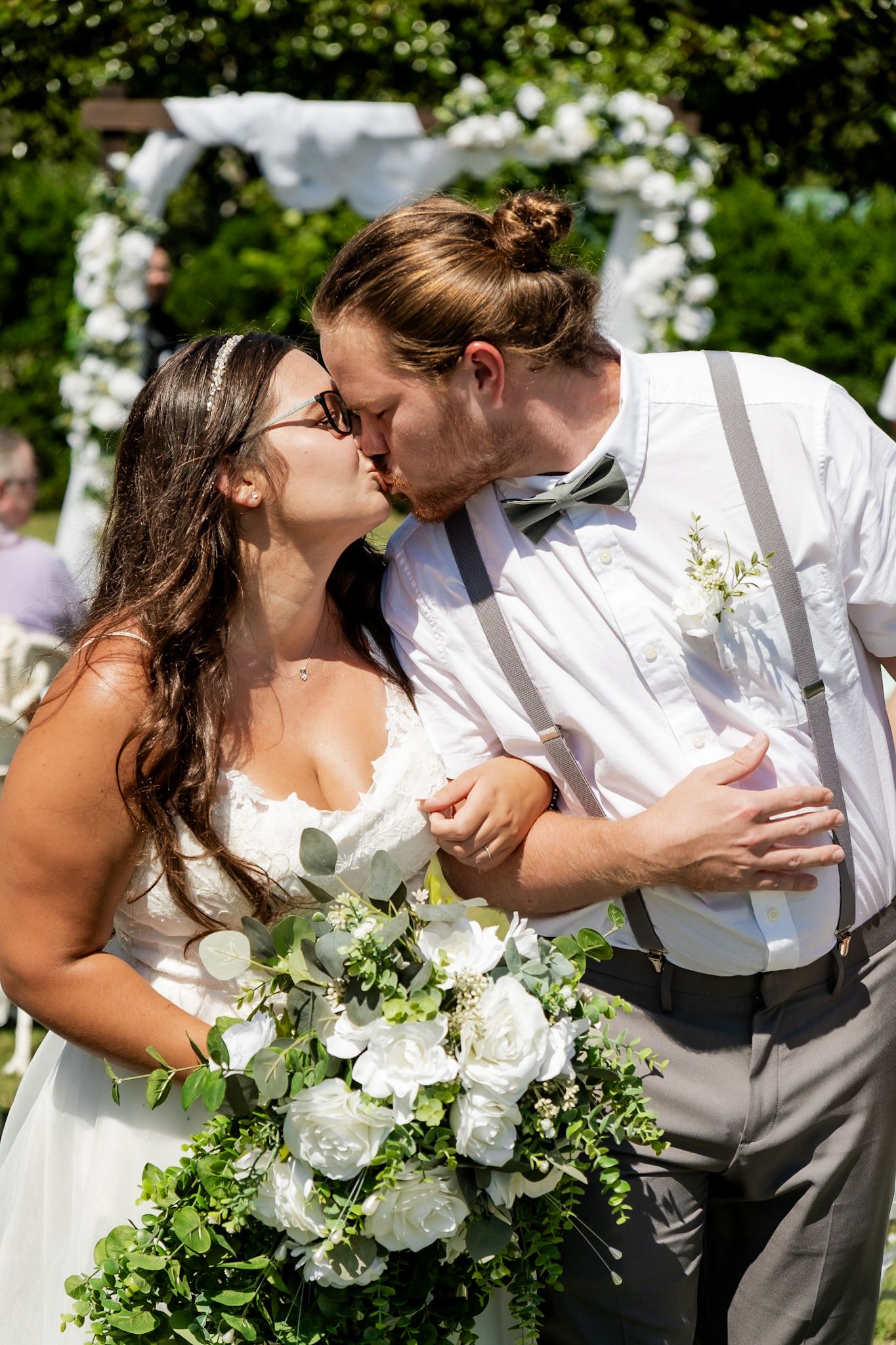 A romantic wedding day kiss shared under a floral archway with white bouquet.