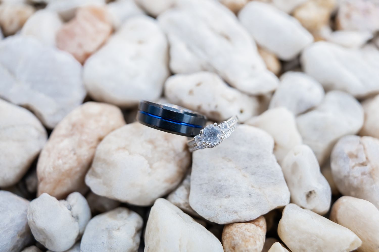 Wedding rings displayed on smooth white and pink stones with blue accents.