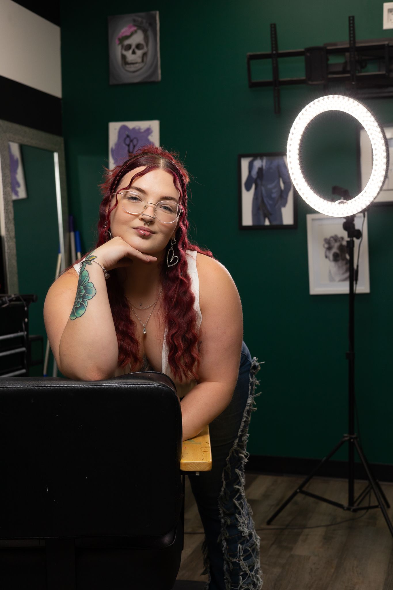 In a photography studio with green walls and a ring light, someone poses thoughtfully in front of artwork and decor.
