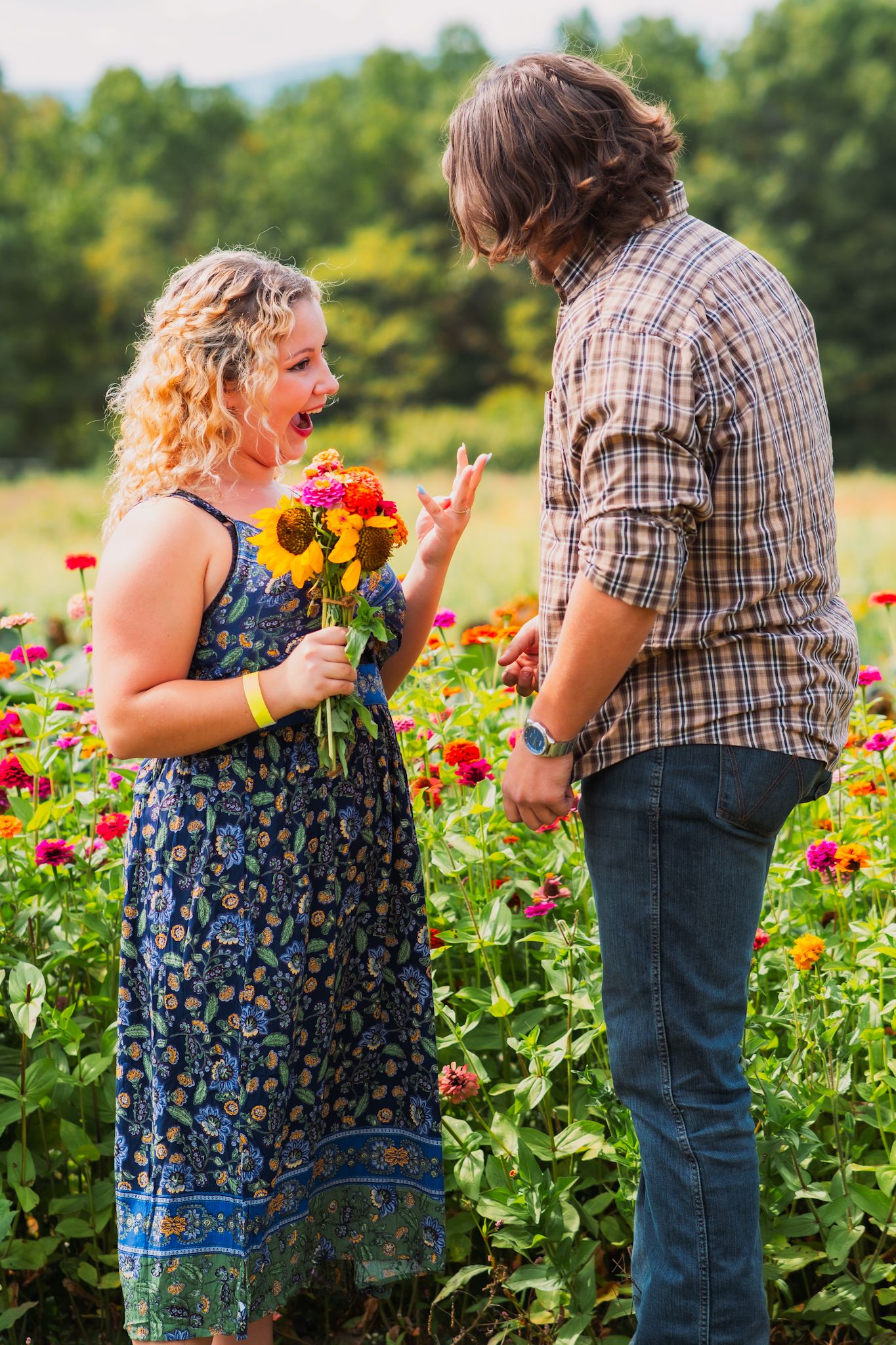 A couple shares an animated conversation in a flower garden while holding a bouquet of sunflowers.