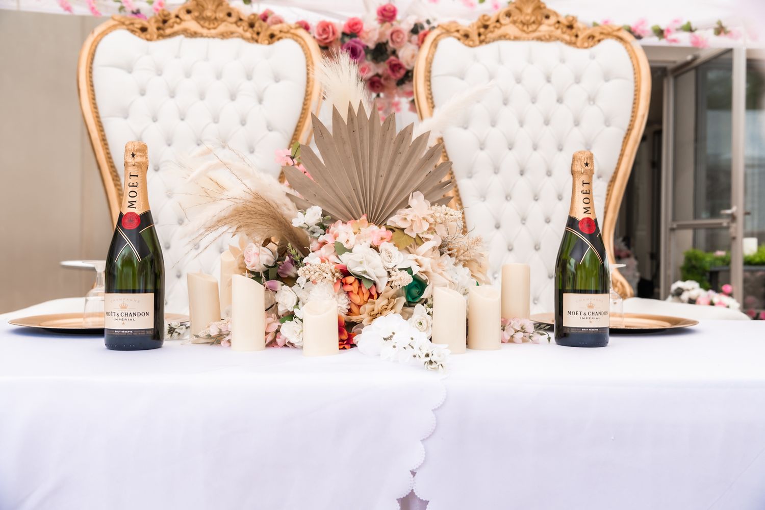 Elegant white tufted chairs with gold trim and champagne bottles set for a luxury wedding reception.