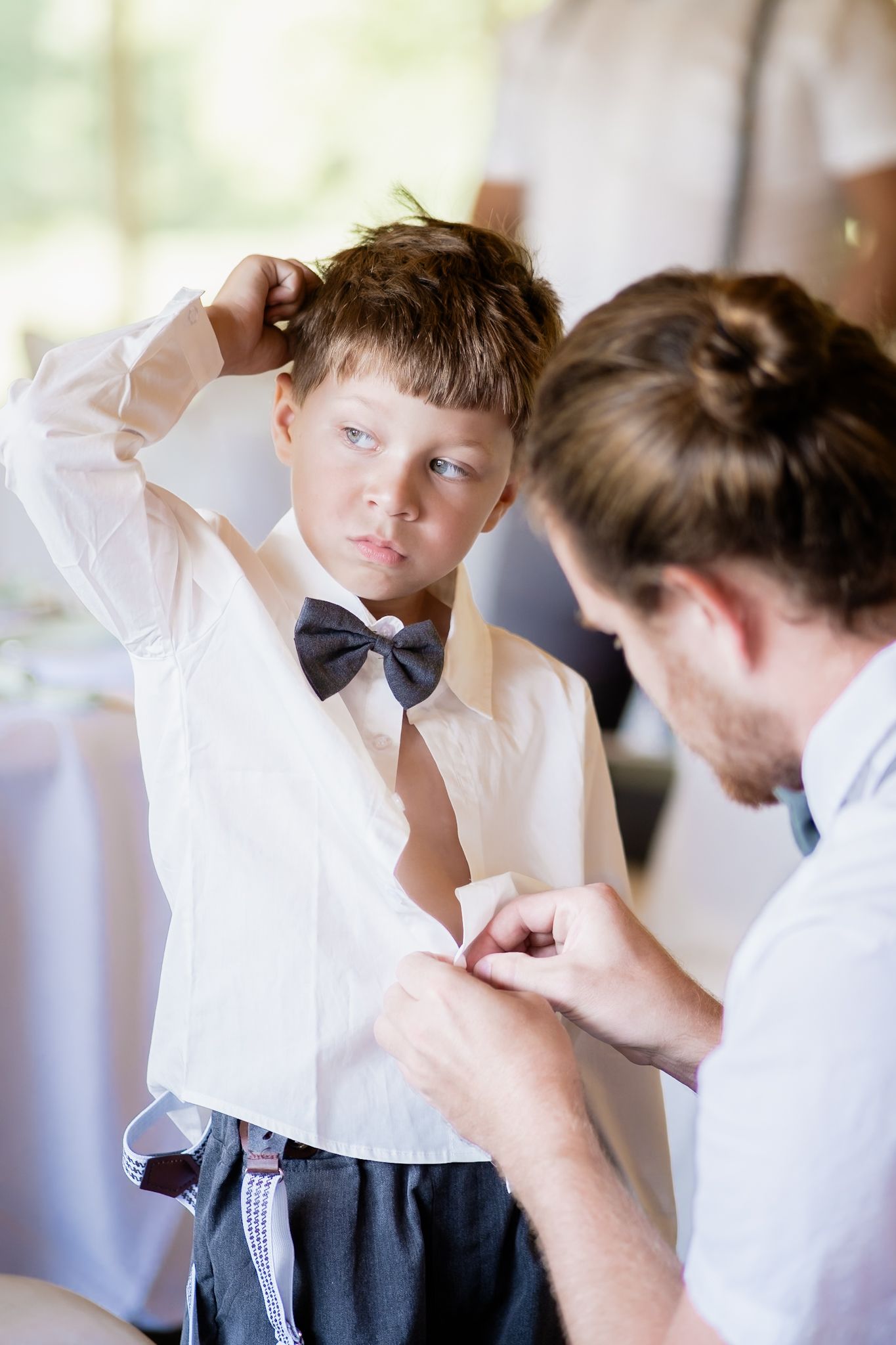 Young attendant getting dressed in formal attire with assistance.