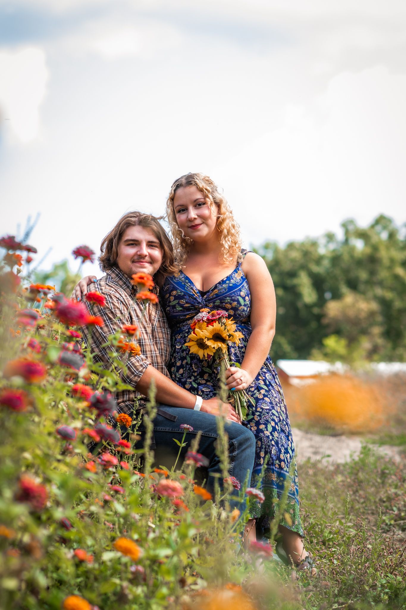 Two people smile warmly at the camera while embracing in a wildflower garden.
