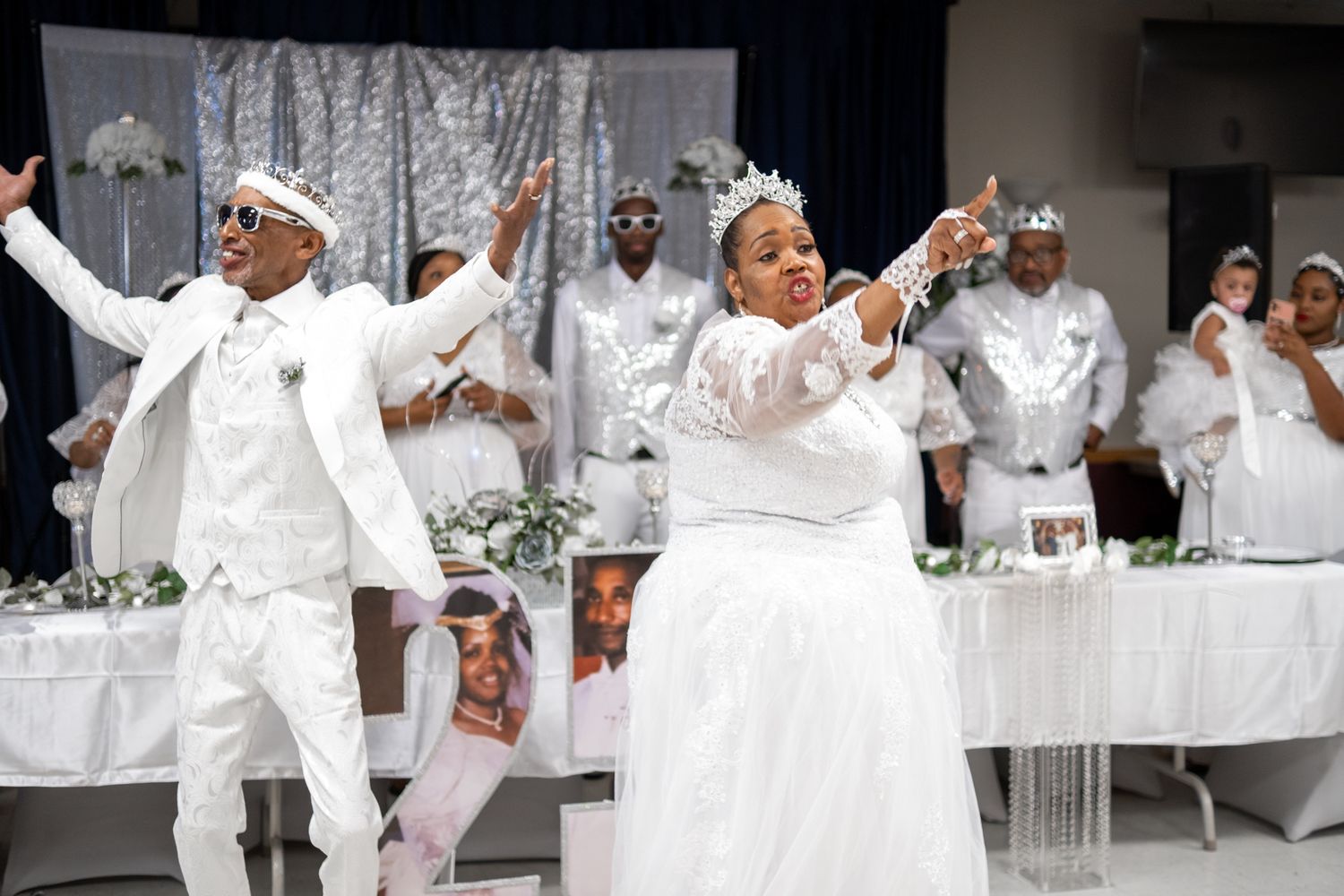 Dancing celebration scene with people in all-white outfits performing choreographed moves at a festive event.