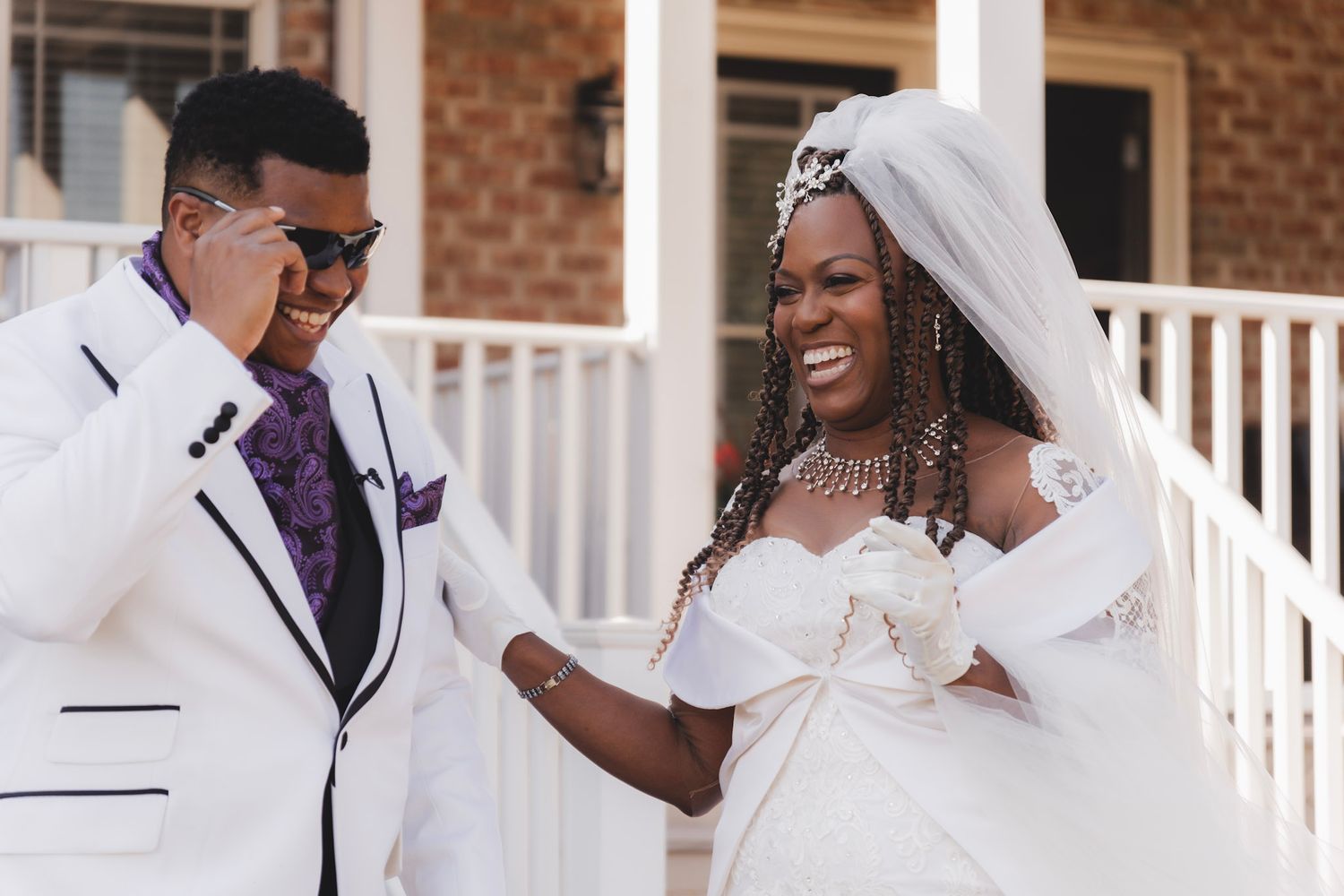 Bride and groom sharing candid moment on porch in white and purple wedding attire.