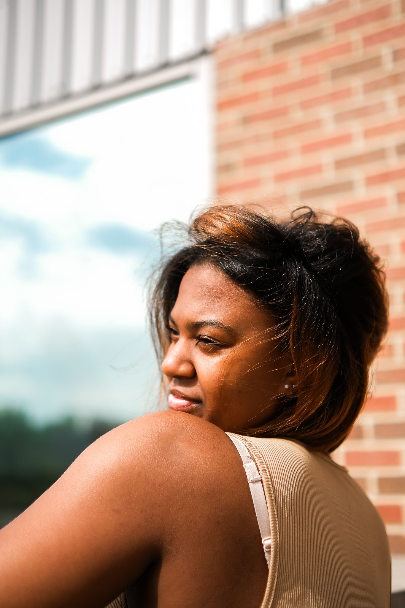 Profile shot of someone with short highlighted hair looking over their shoulder on a sunny day against a brick wall.