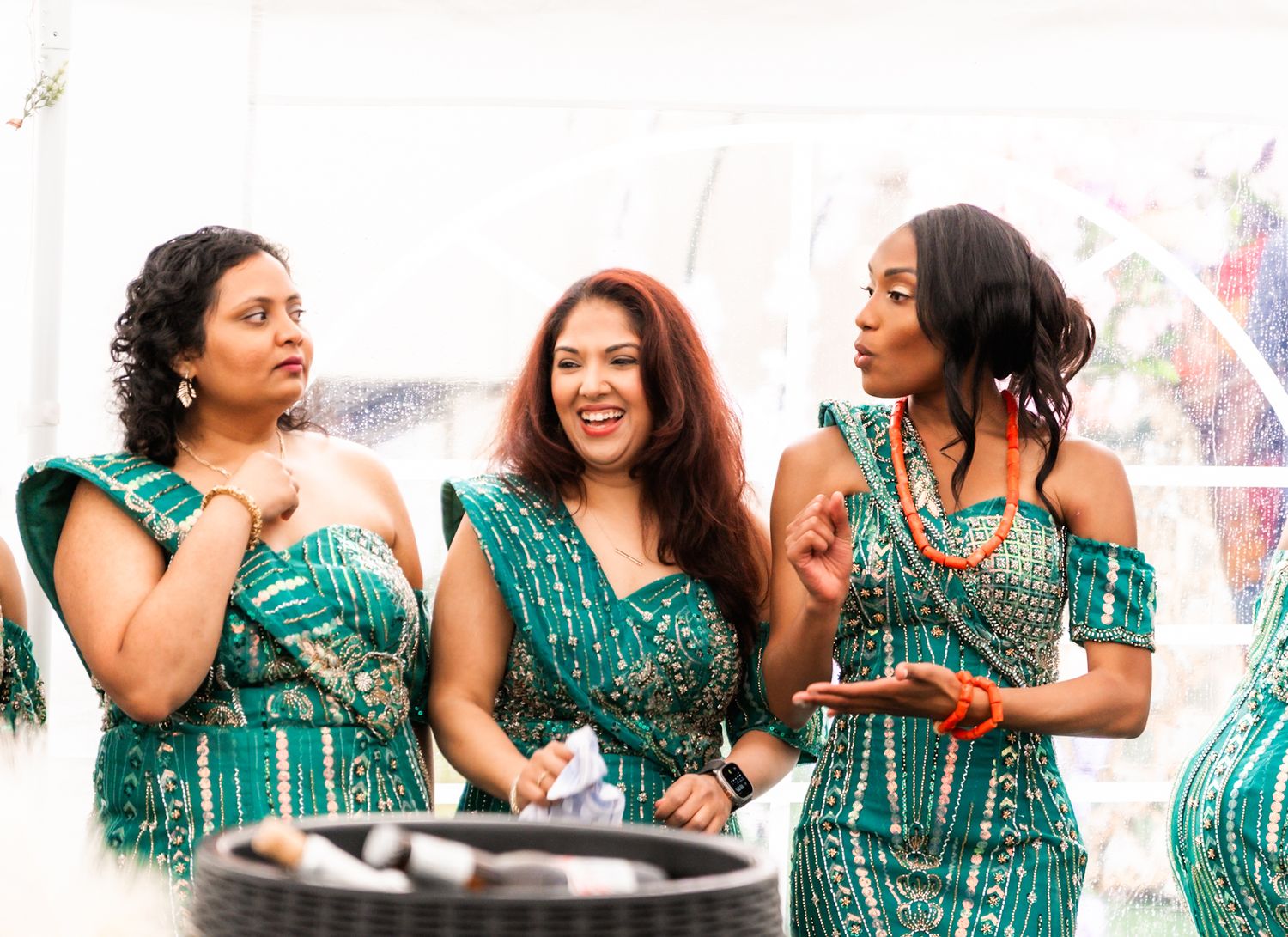 Friends in matching turquoise dresses laughing together at an outdoor event.