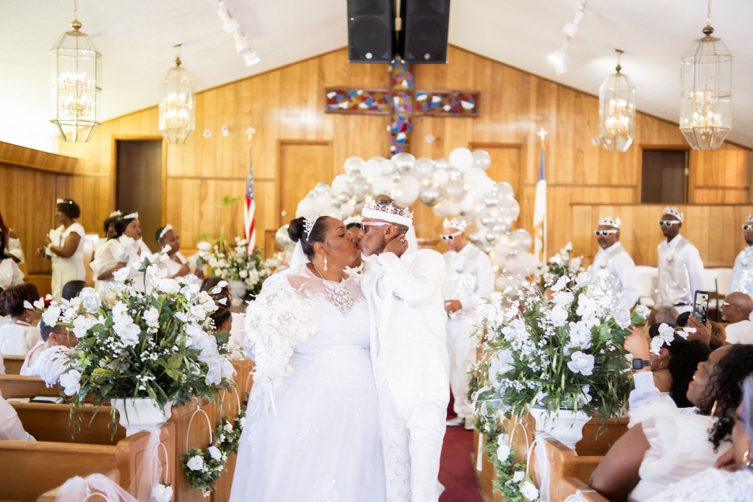 Beautiful church wedding ceremony decorated with white floral arrangements and candle lanterns in a wooden chapel interior.