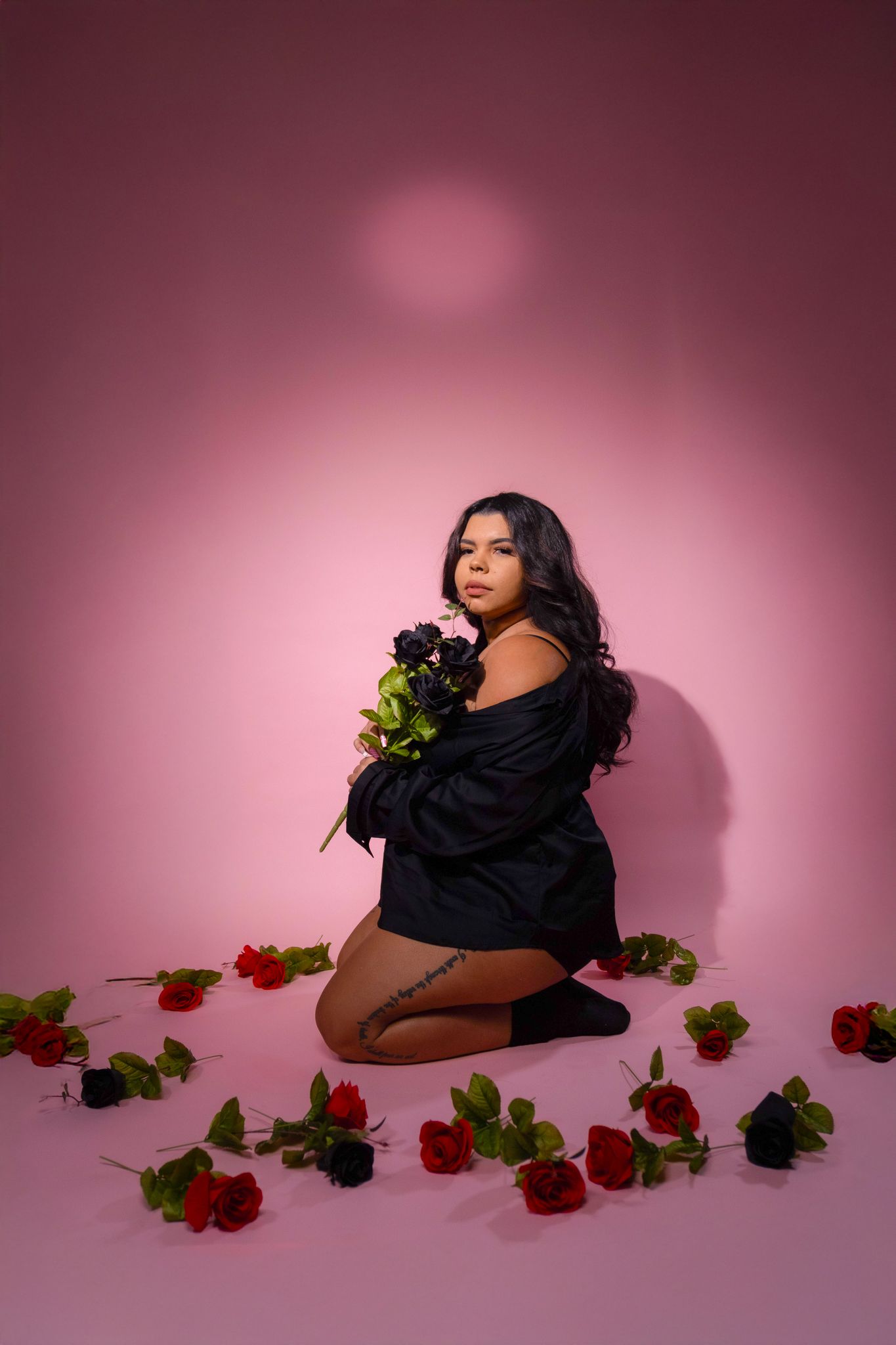 Romantic photoshoot with scattered red roses on pink background featuring black attire.