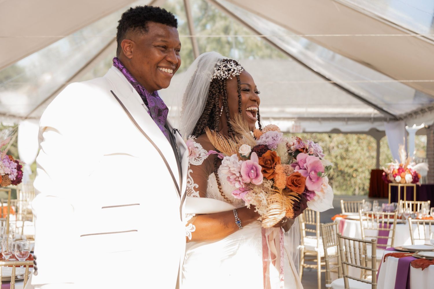Newlyweds share a joyous moment under a white tent with pink floral bouquets.