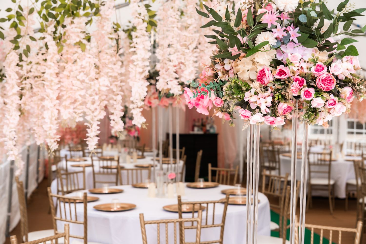 Romantic wedding reception setup with hanging flowers, pink blooms and gold chiavari chairs.