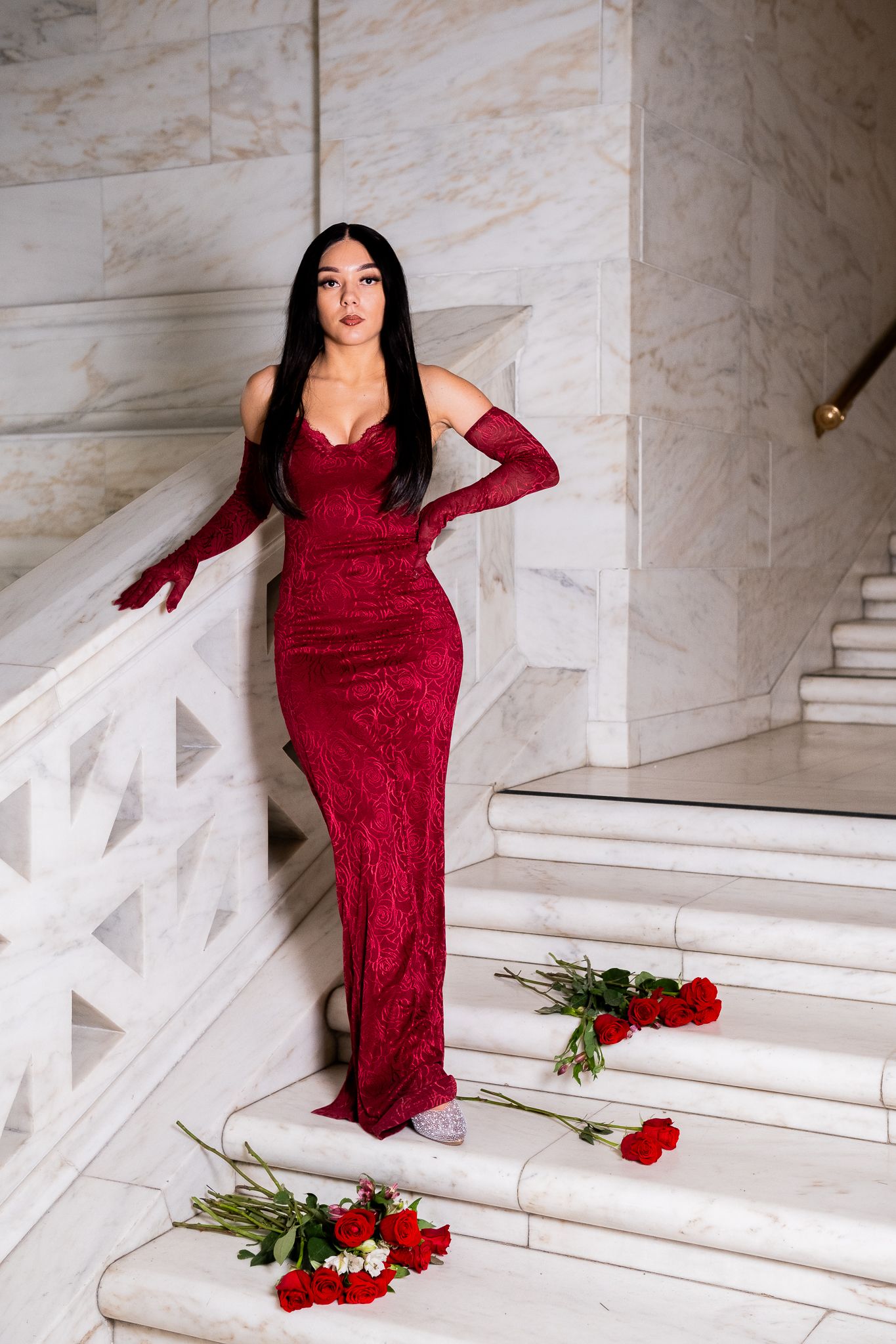 Full length fashion shot in red evening gown on marble stairs with floral accents.