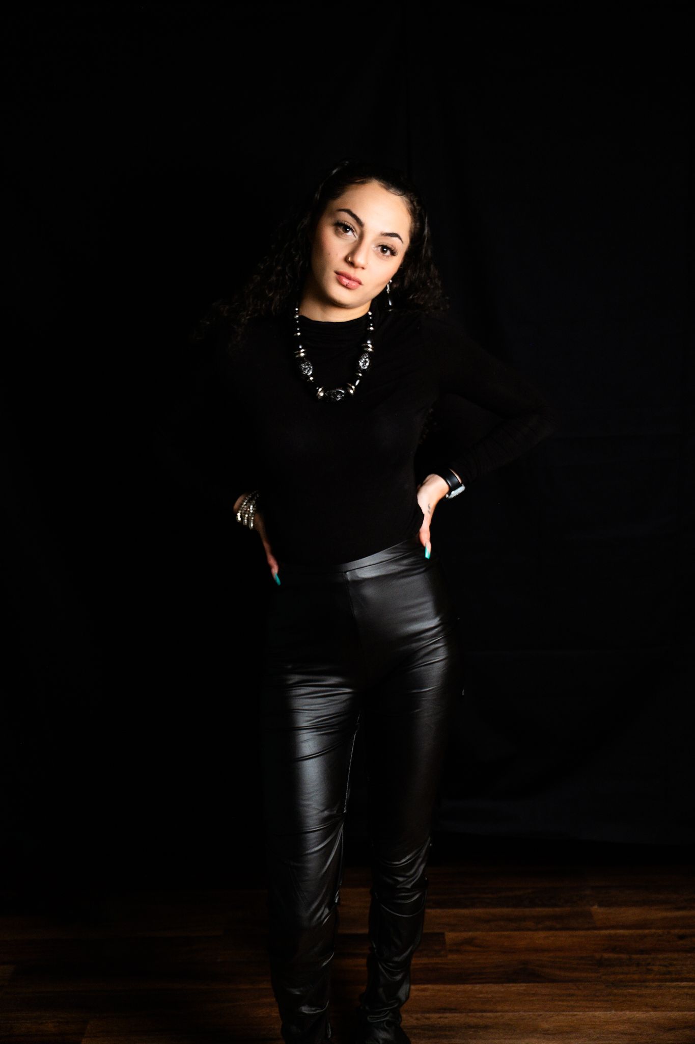 Stylish pose in black outfit with statement necklace against dark background.