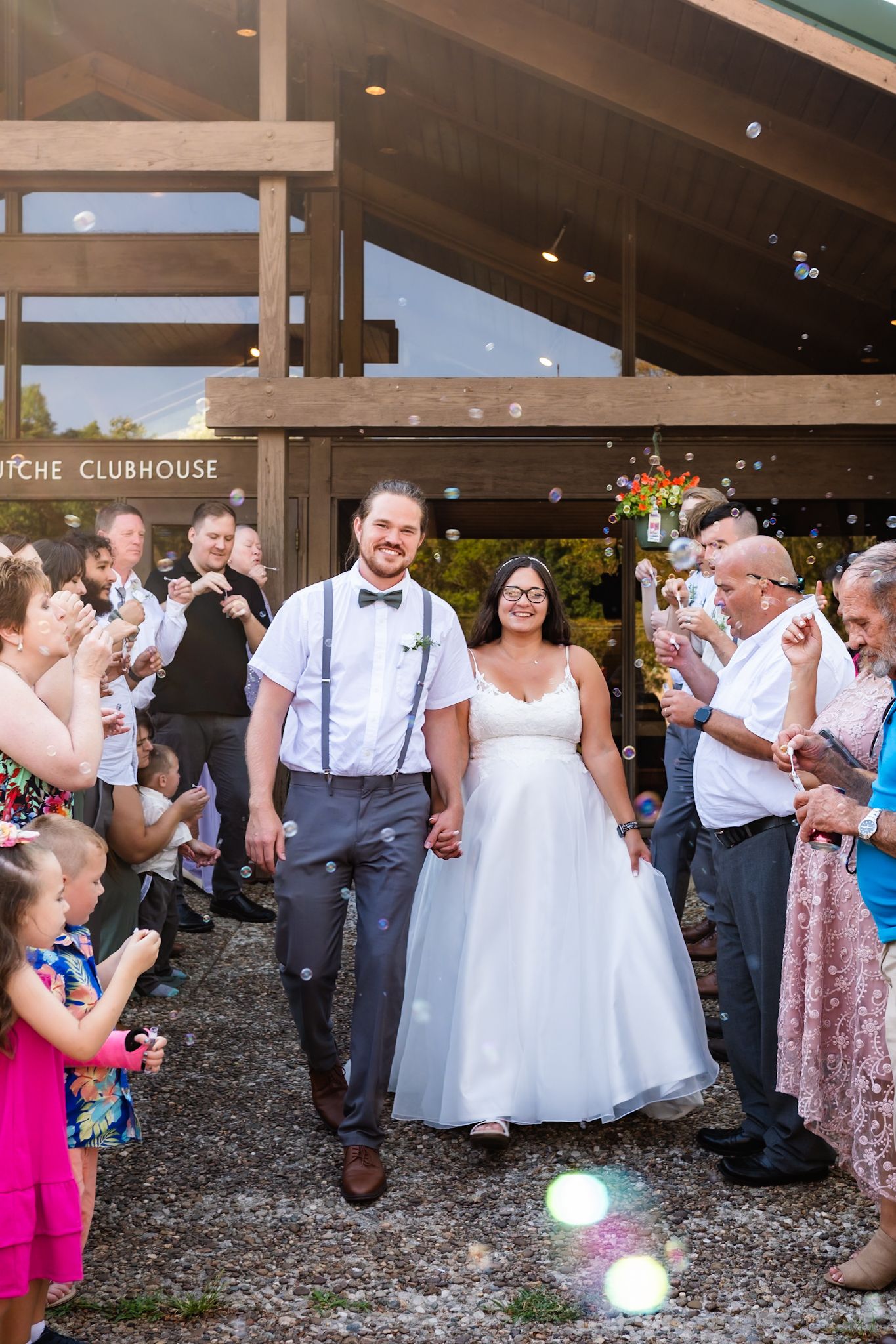 Newlyweds exit through a crowd of guests blowing bubbles outside a rustic clubhouse.