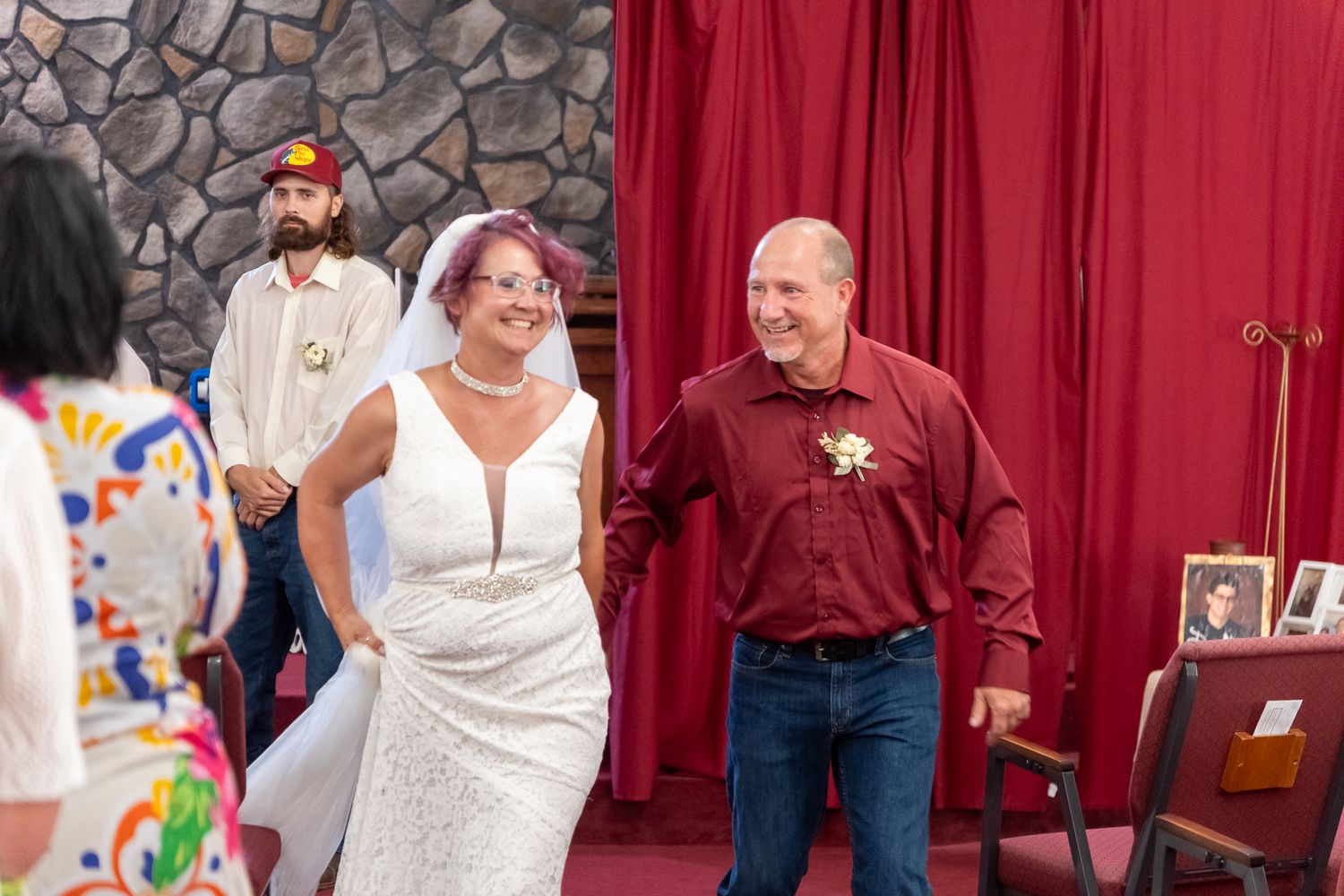 A person in a white wedding gown dances joyfully with someone wearing a red shirt at an indoor reception.