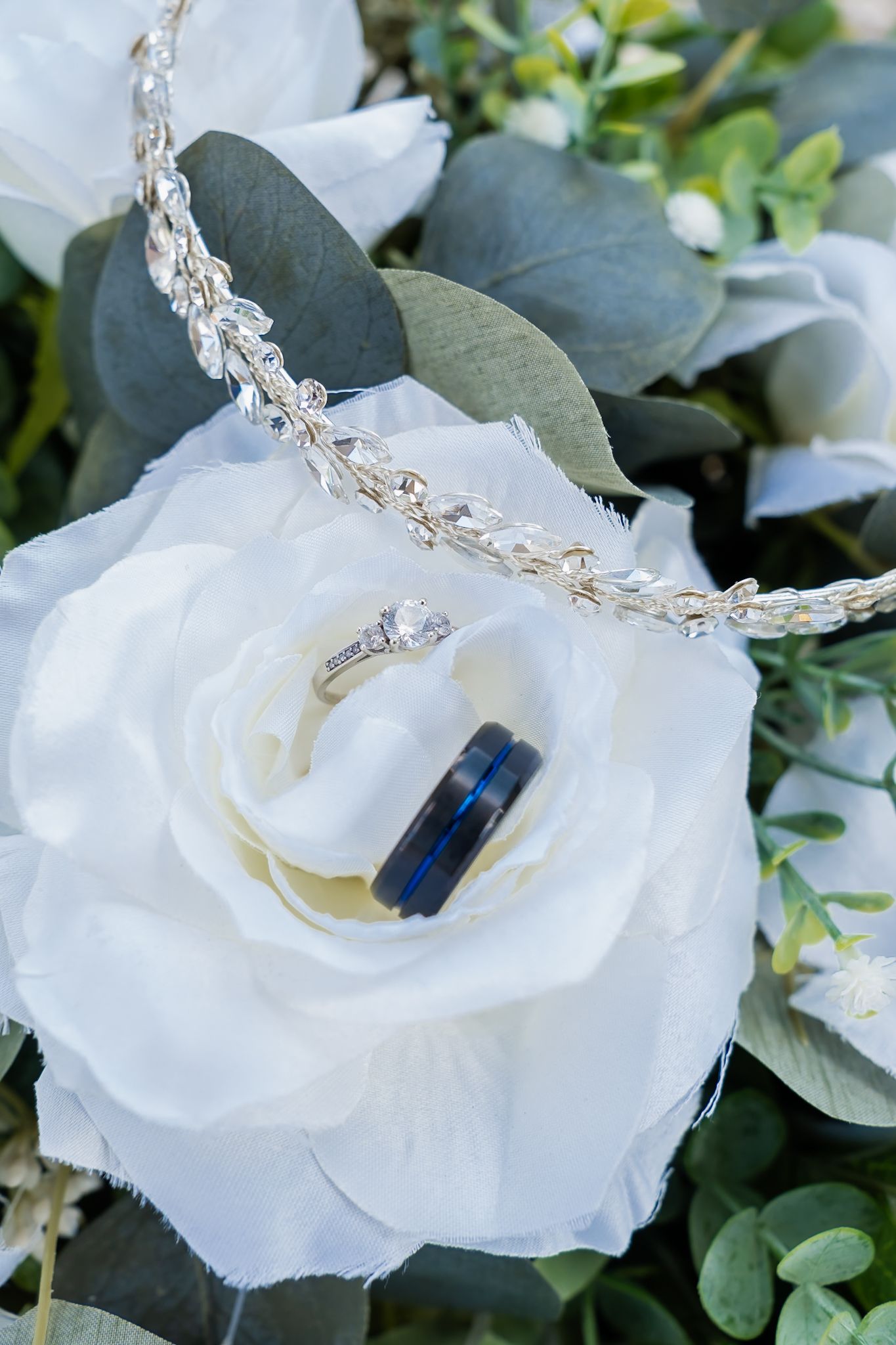 Wedding rings and crystal headpiece artfully arranged on a white rose with eucalyptus leaves.