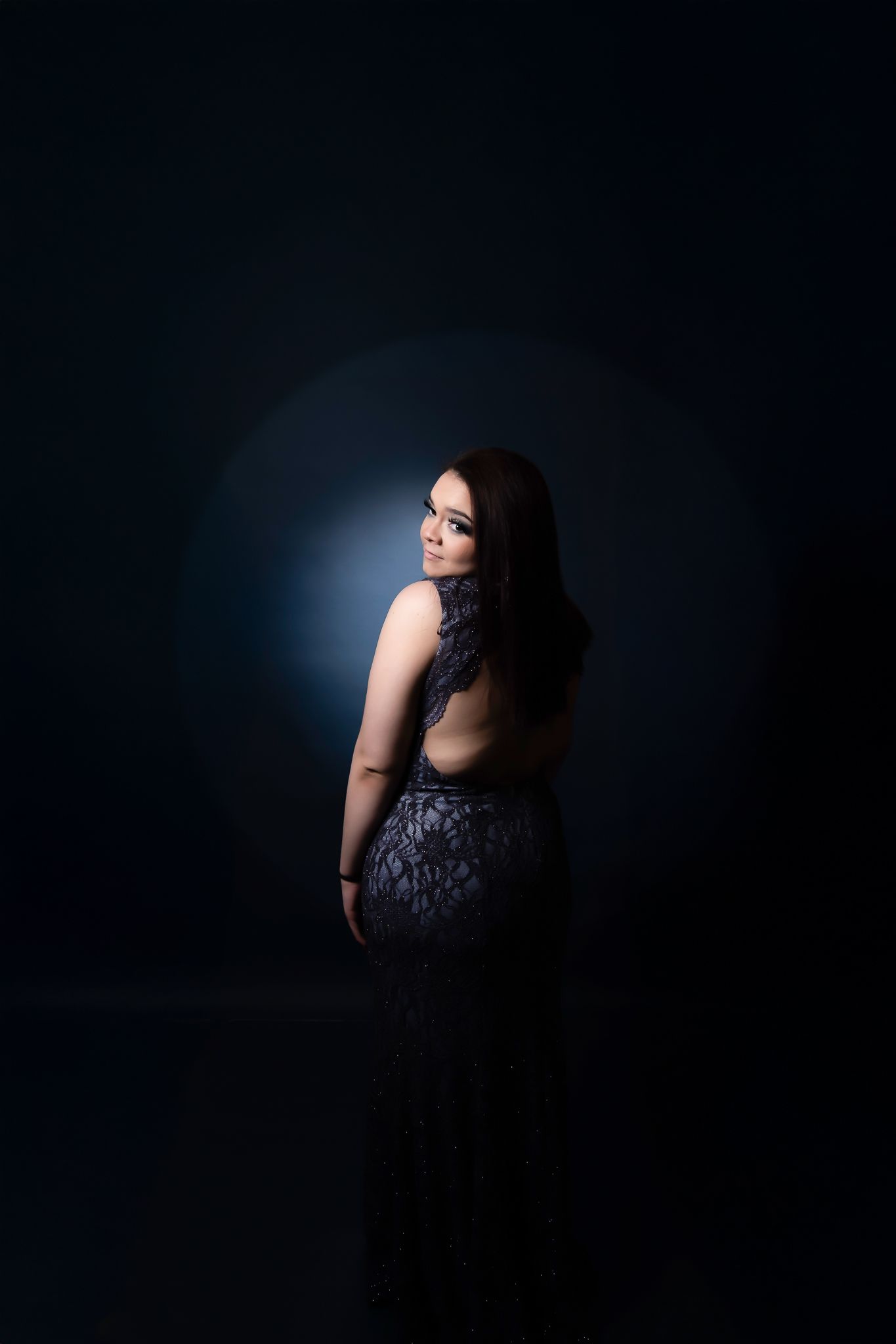 Dramatic portrait of a figure in a lace dress against a dark background with moody blue lighting.
