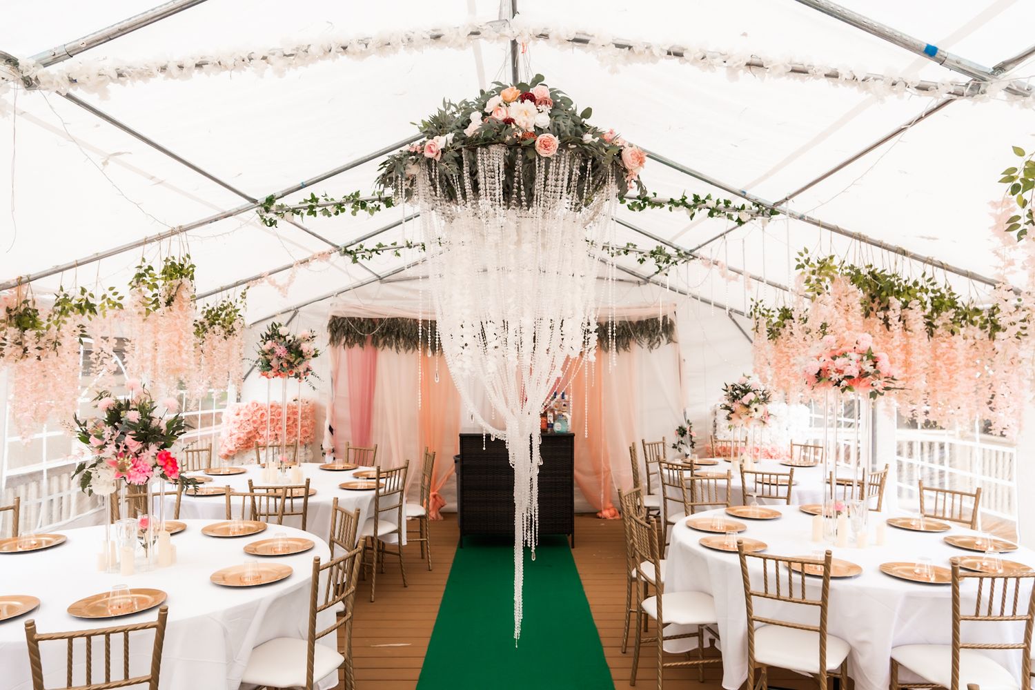 Wedding reception tent decorated with hanging crystals, pink draping and white chiavari chairs.