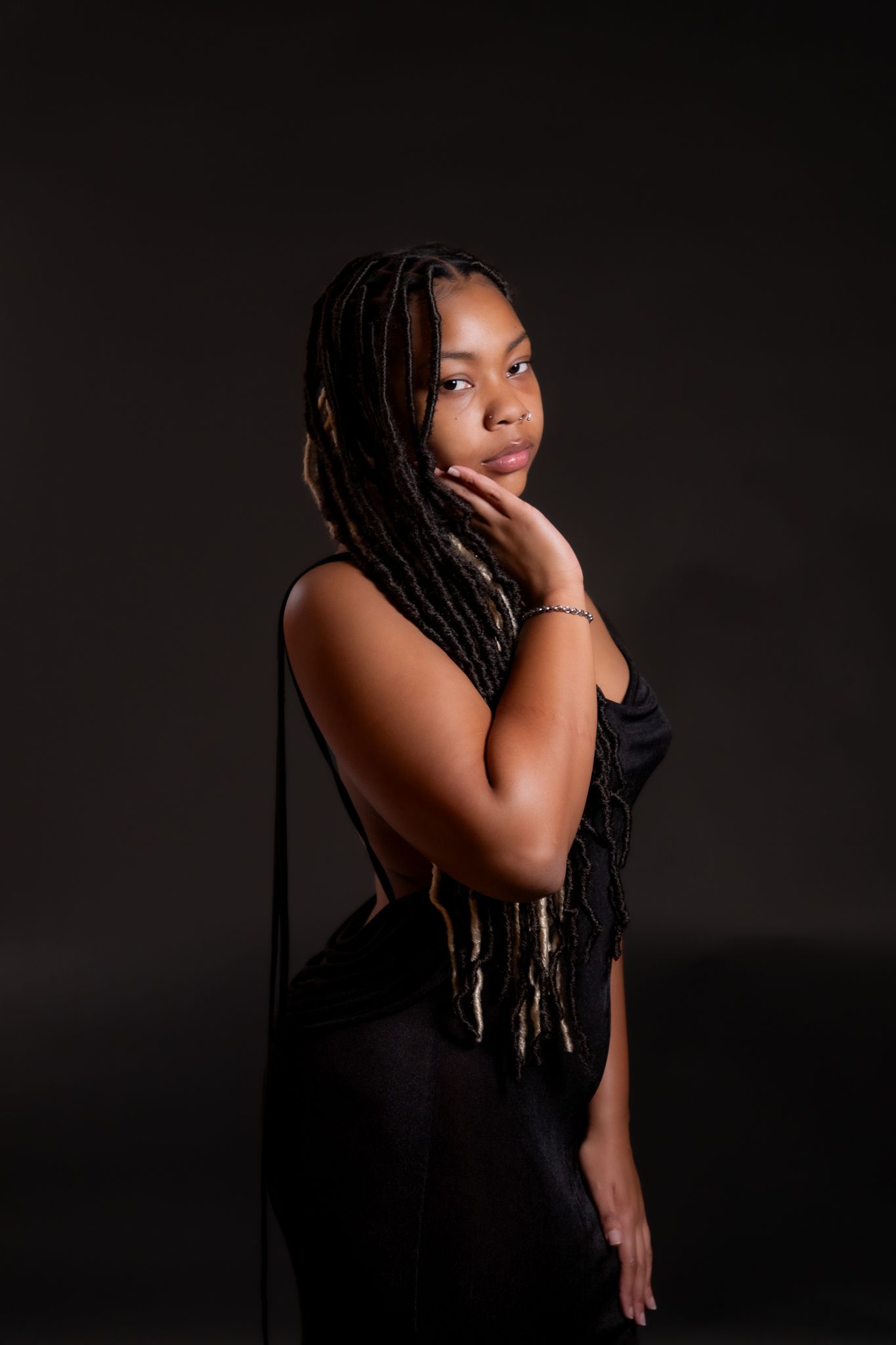 Artistic portrait against dark background featuring dramatic lighting and long braided hair.
