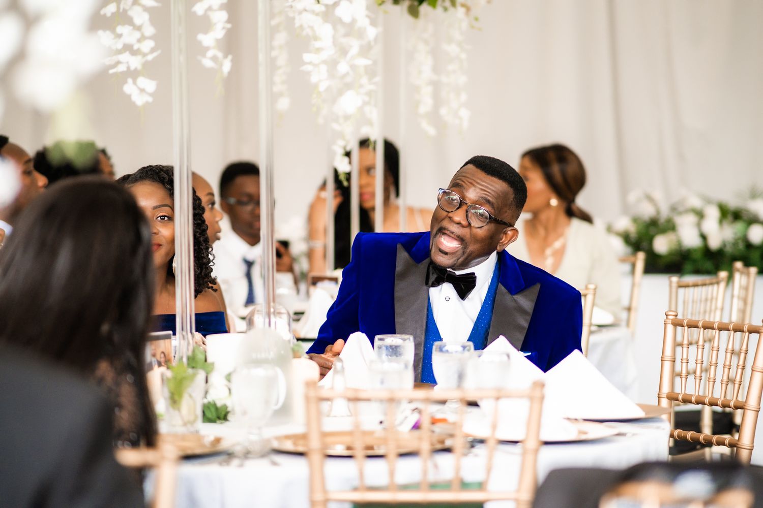 Wedding reception scene with guests seated at decorated table.