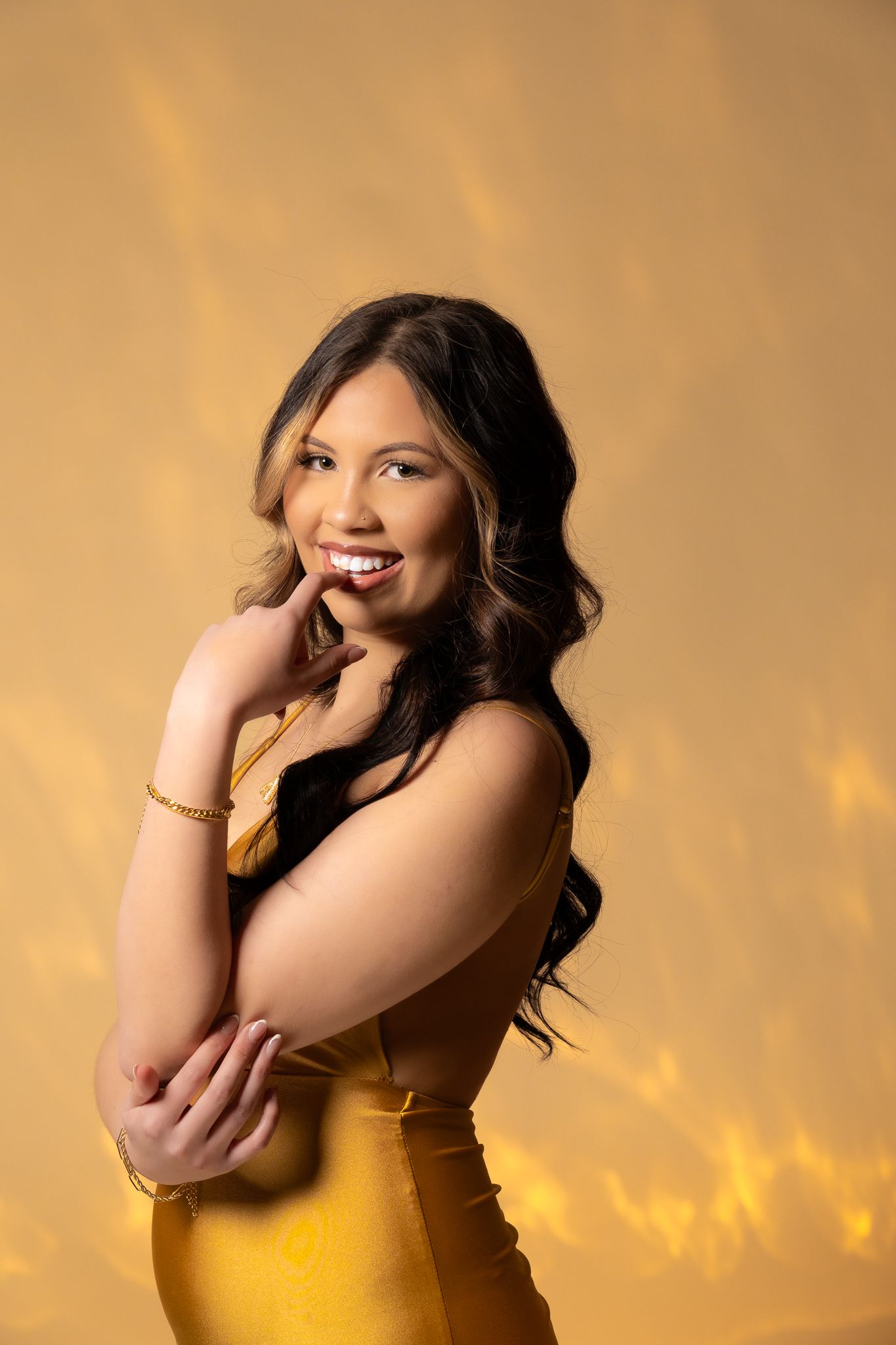 Portrait against golden background showing elegant pose in yellow dress with warm lighting and a bright smile.