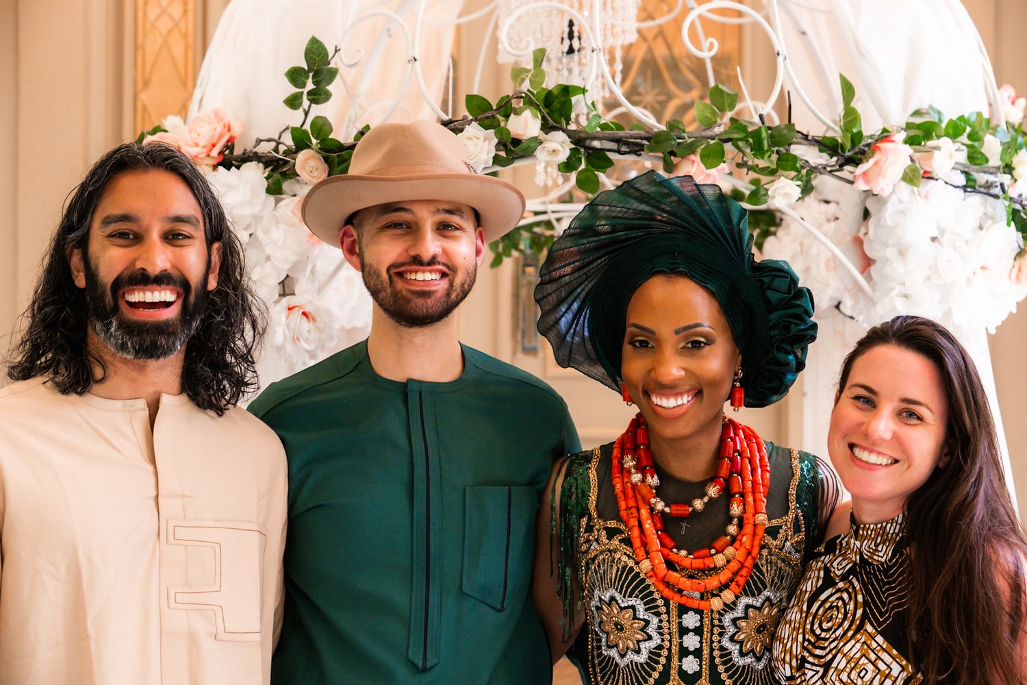 Group poses under a floral wedding arch with traditional African-inspired attire.