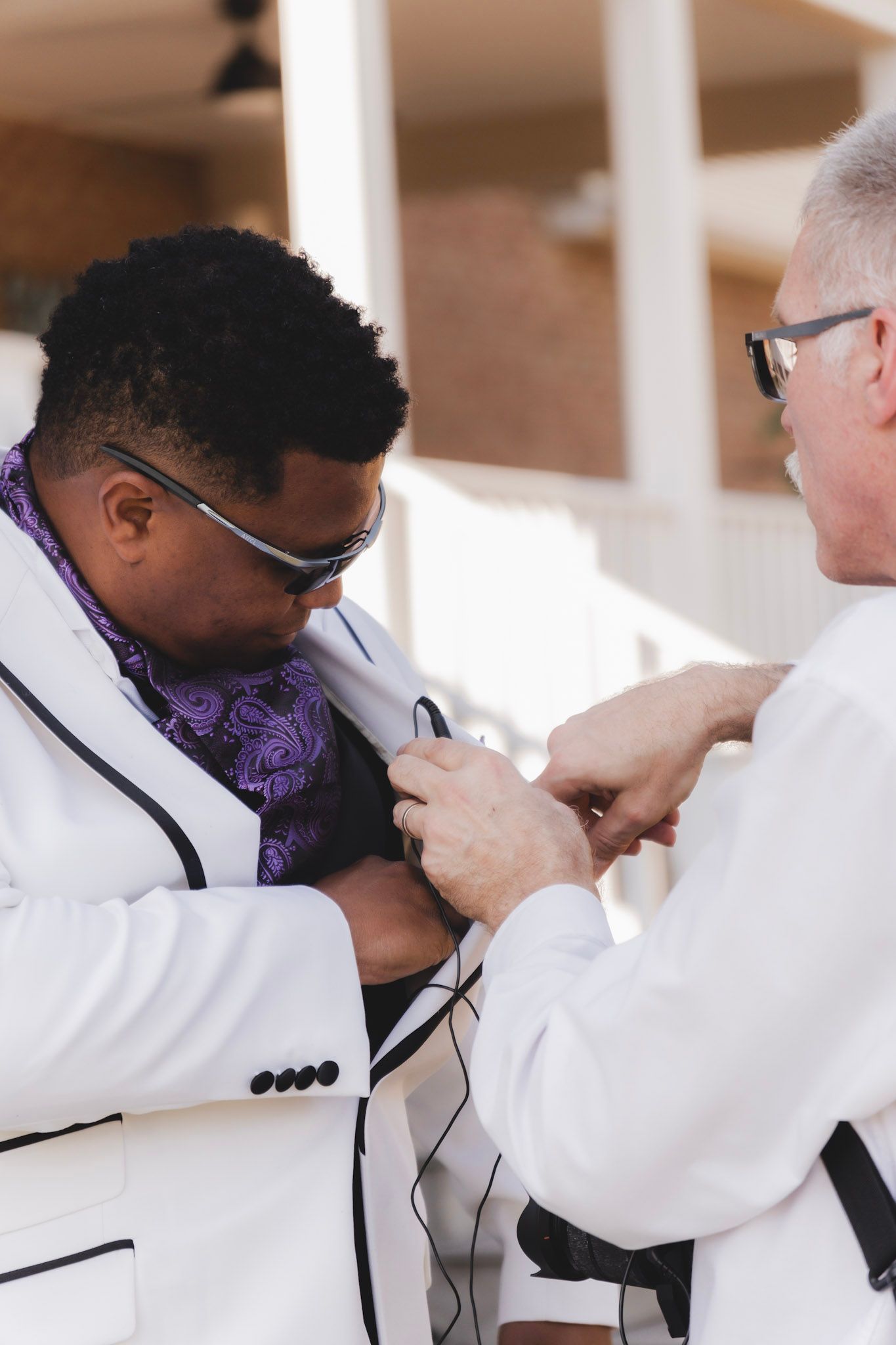 Two people in formal wear adjusting boutonniere during wedding preparation.