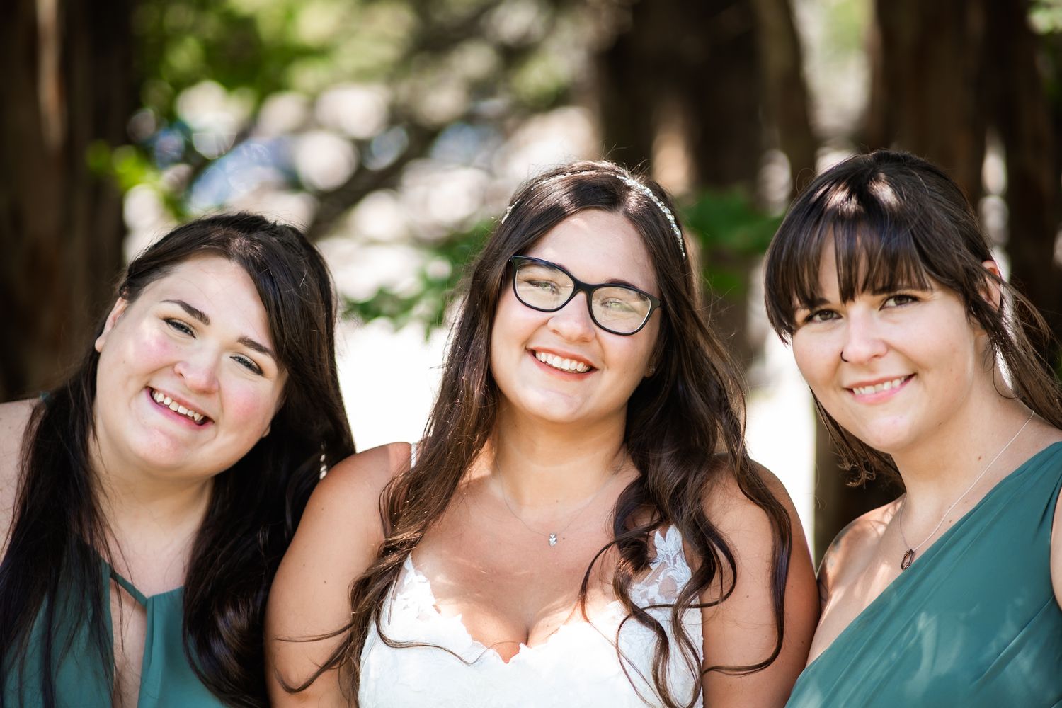 Three friends share laughter and smiles during a wedding celebration outdoors.