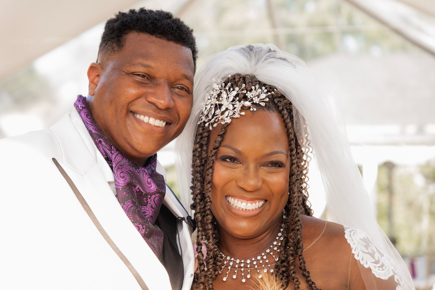 A wedding portrait showing radiant smiles and elegant attire under a clear tent.